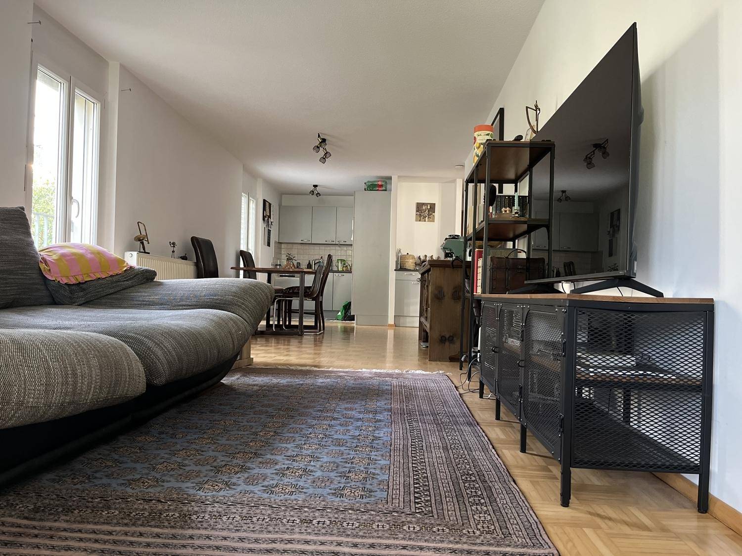 Möblierter Wohnbereich mit Sofa, Teppich und Blick auf den Essbereich und die Küche.