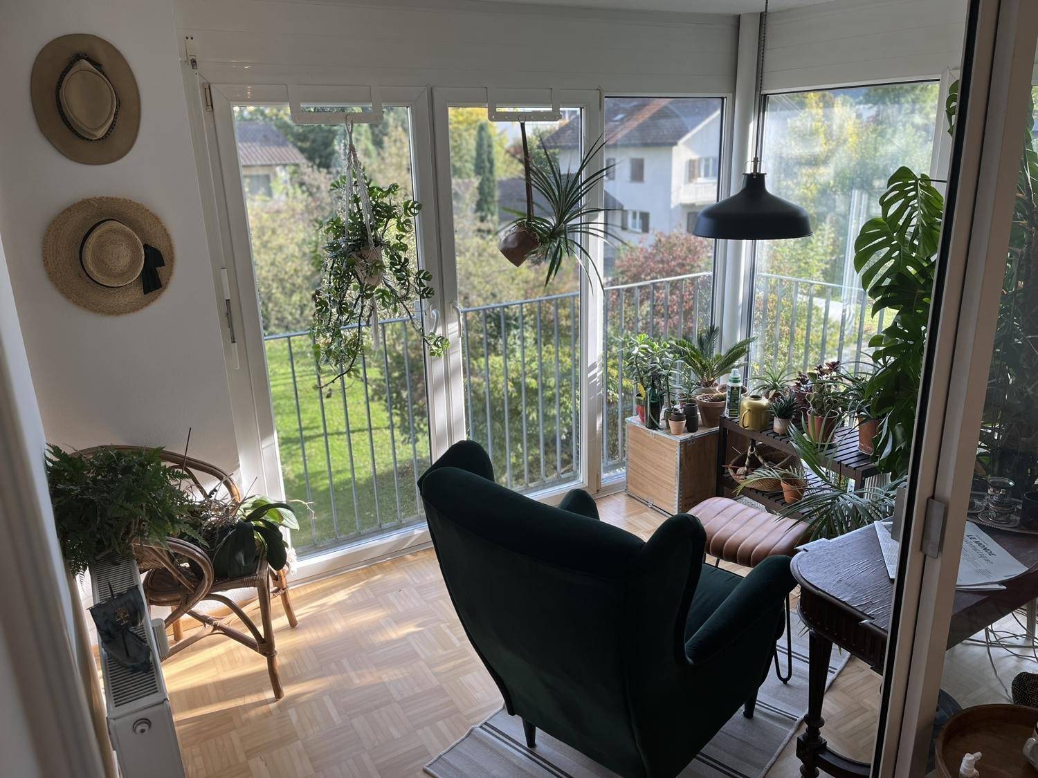Gemütliche, verglaste Loggia mit vielen Pflanzen, Sessel und Blick ins Grüne.
