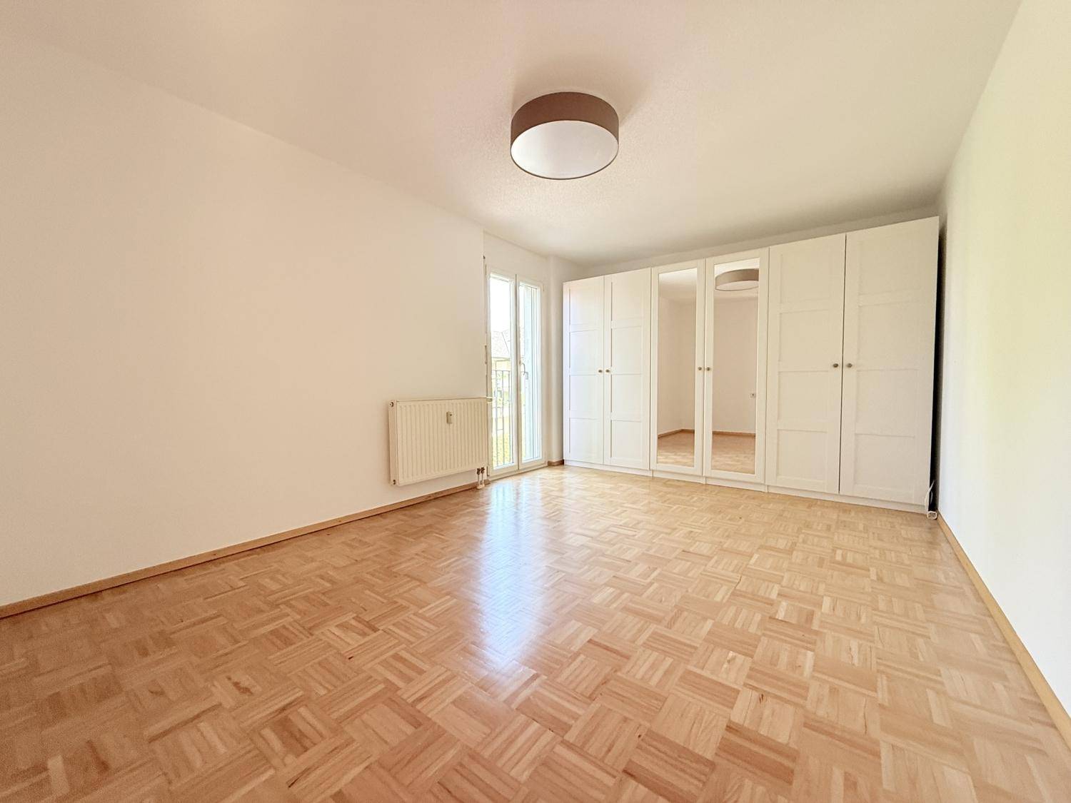 Geräumiges Schlafzimmer mit Parkettboden, weißem Einbauschrank und Zugang zum französischen Balkon.