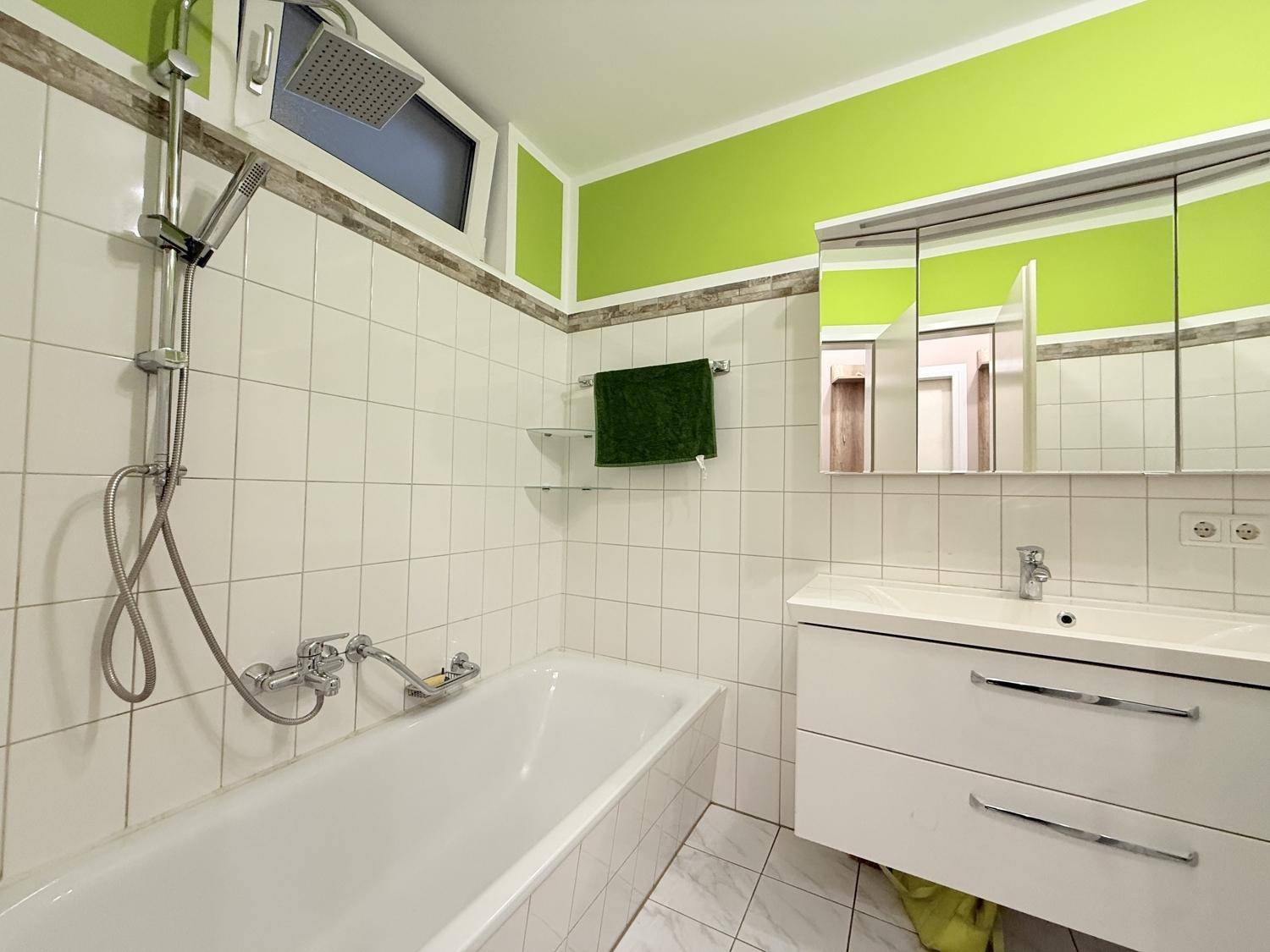 Helles Badezimmer mit Badewanne, integrierter Dusche und Waschtisch mit Spiegelschrank.