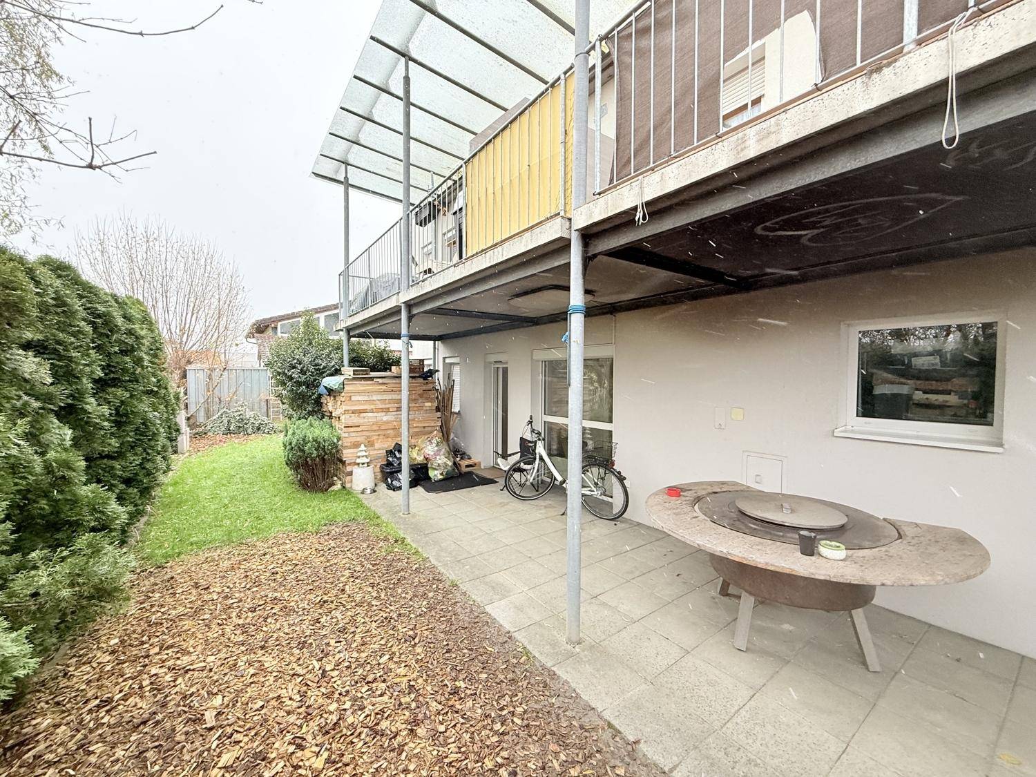 Gartenbereich mit Terrasse, Rasenfläche, Hecken und einem Balkon im Obergeschoss des Hauses.