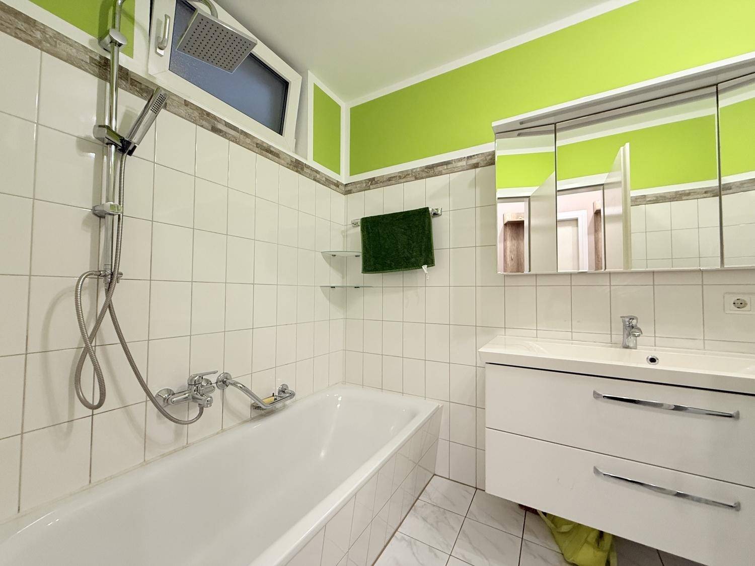 Badezimmer mit Badewanne, Duschfunktion, Waschtisch und einem kleinen Fenster für Tageslicht.