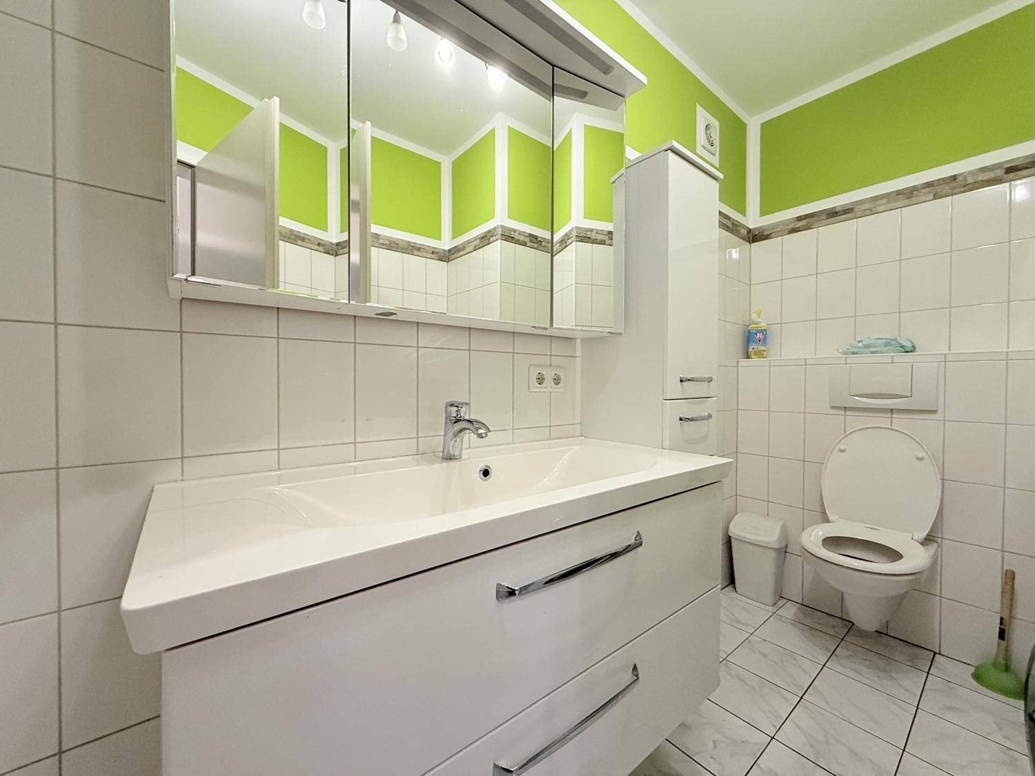 Badezimmer mit grün-weißen Fliesen, modernem Waschtisch und Spiegelschrank über dem Waschbecken.