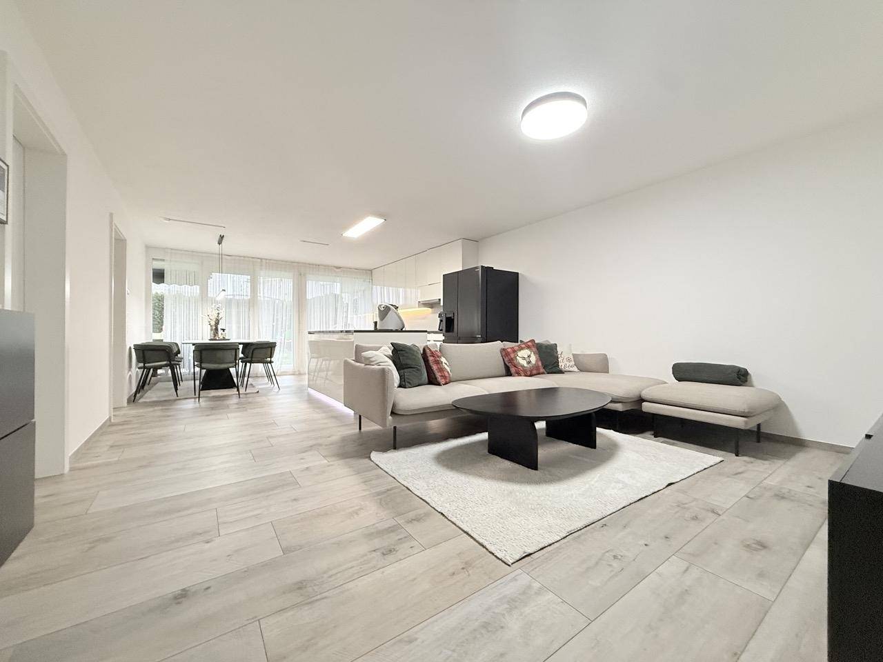 Geräumiger offener Wohnbereich mit beigem Sofa, Couchtisch und Essbereich im Hintergrund.