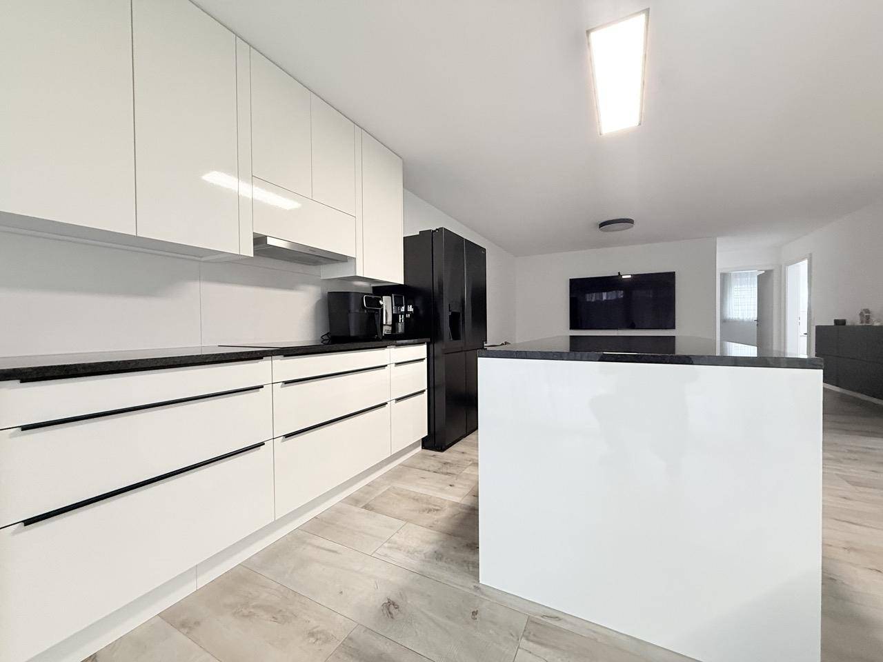 Moderne weiße Küche mit Kochinsel, schwarzen Arbeitsplatten und integriertem Kühlschrank.