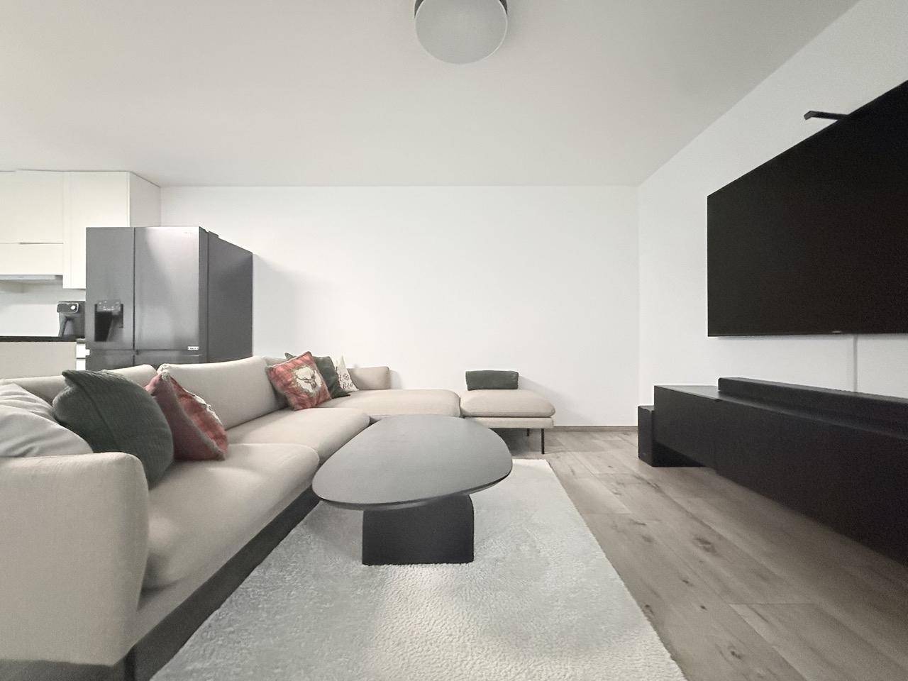 Moderner Wohnbereich mit beigem Ecksofa, Couchtisch und großem Wandfernseher.