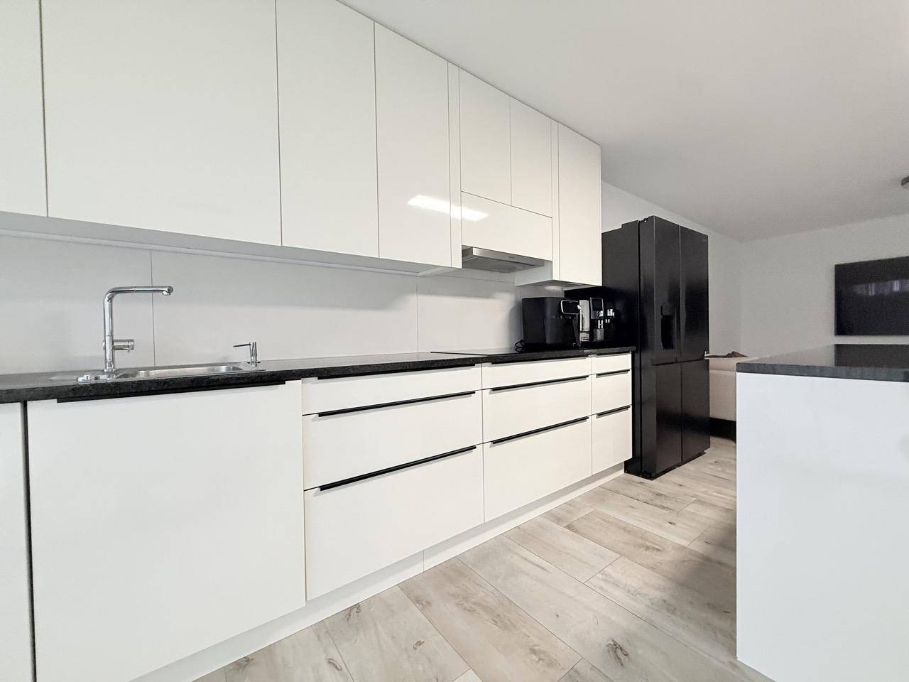 Detailansicht der modernen weißen Küche mit schwarzen Arbeitsplatten und integriertem Kühlschrank.