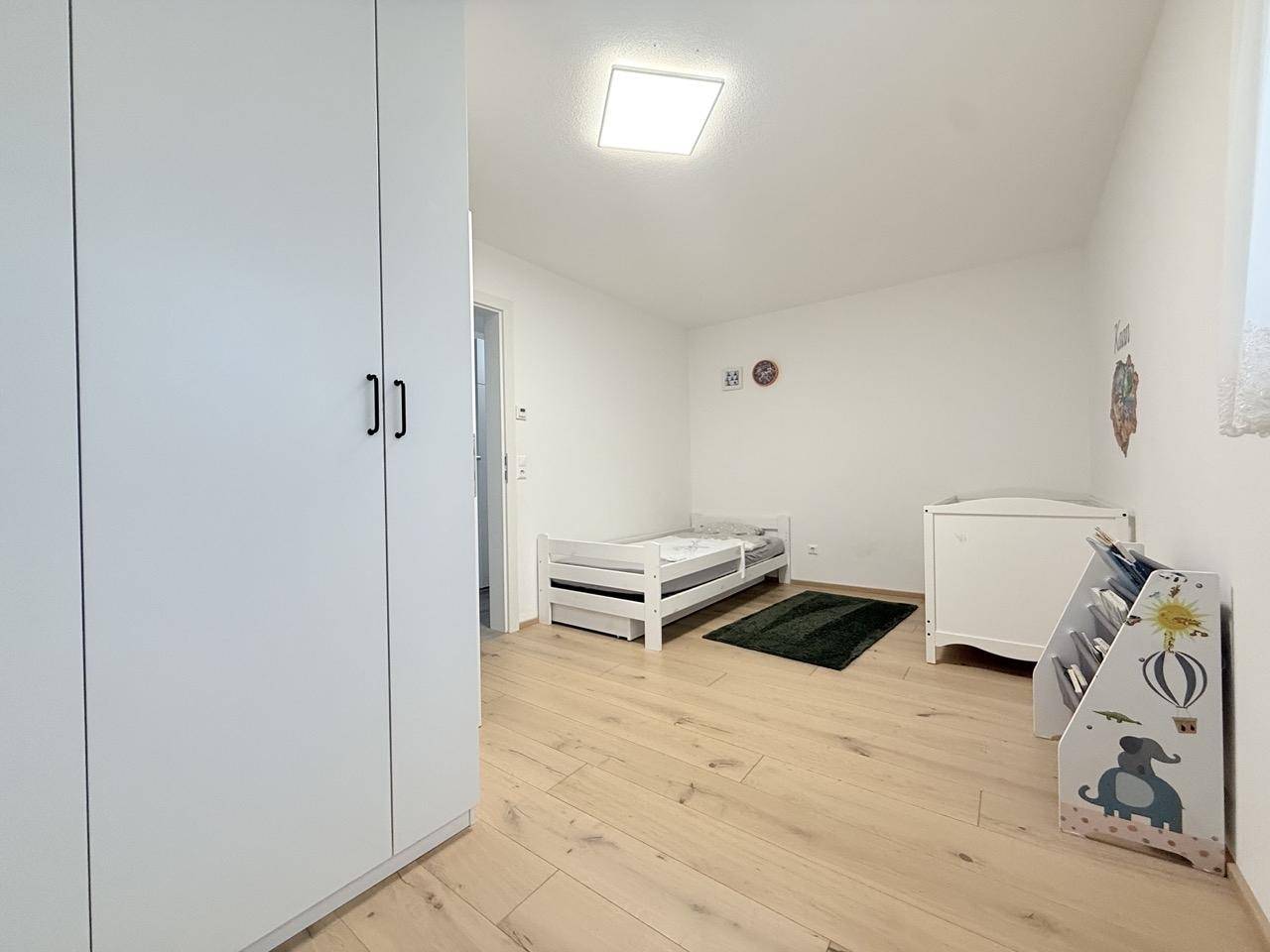 Kinderzimmer mit hellem Holzboden, weißem Kleiderschrank und Babybett.
