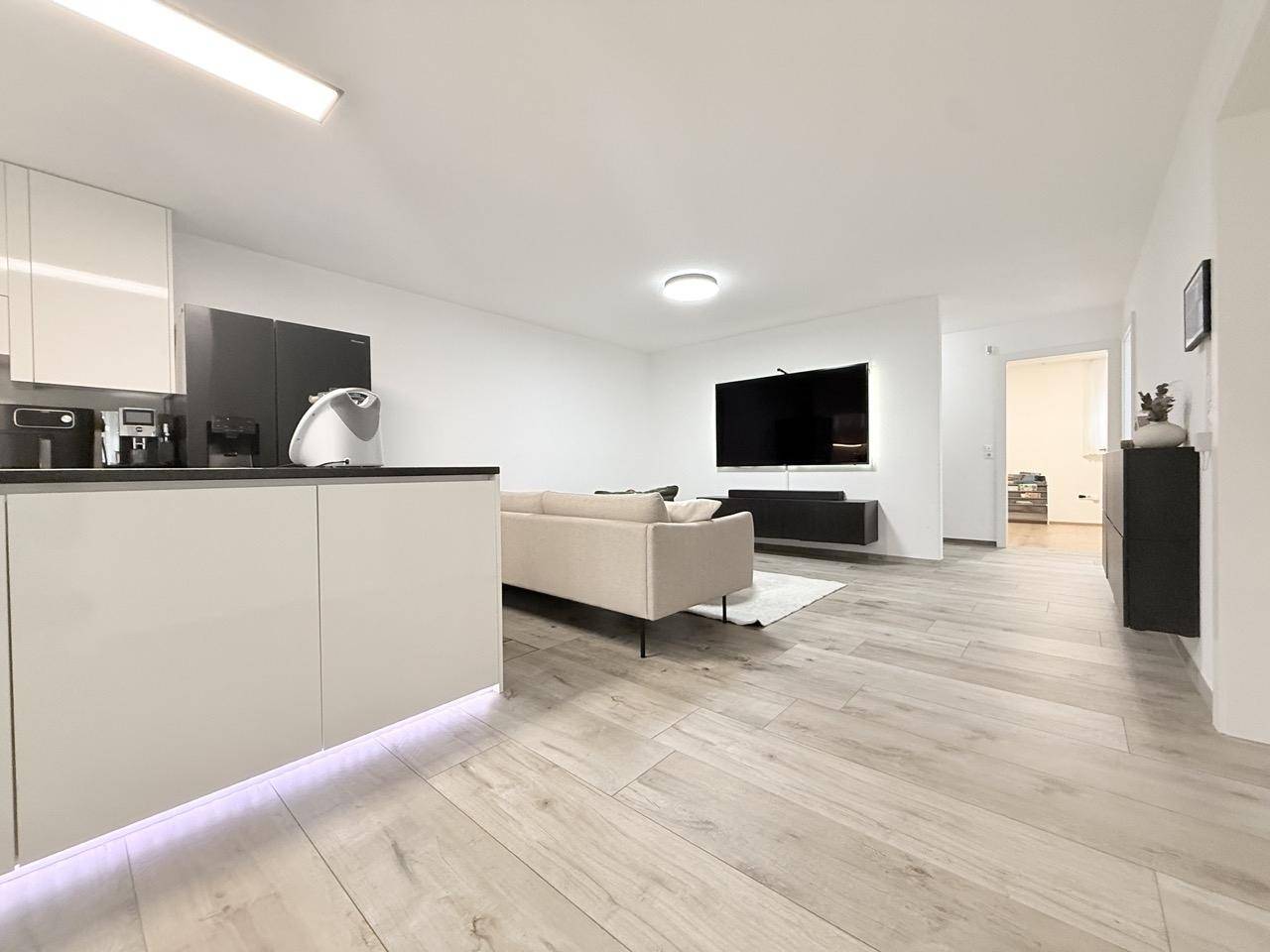 Offener Wohnbereich mit Küche, Sofa und großem Fernseher an der Wand.