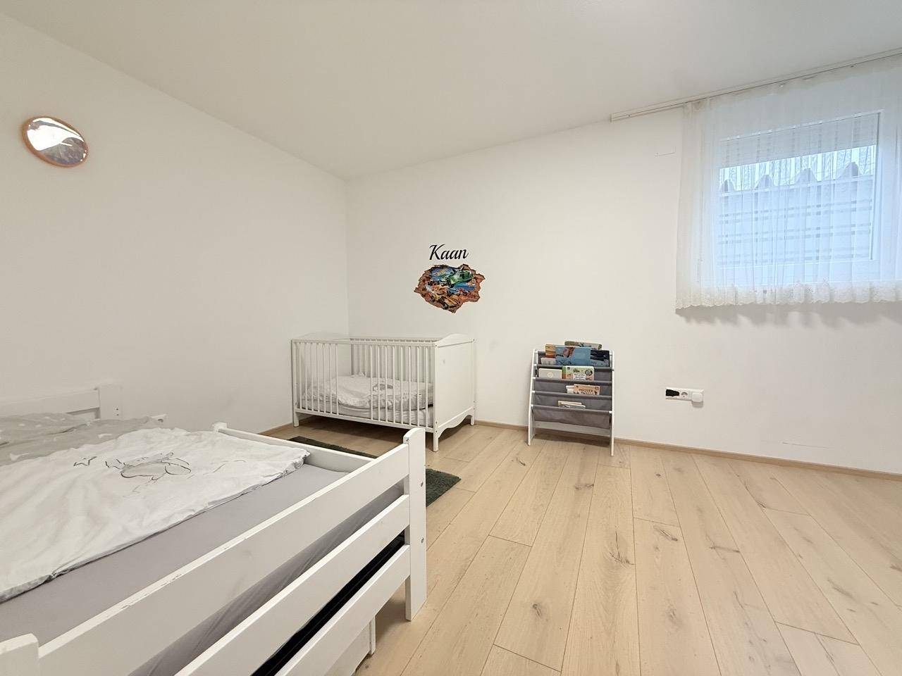 Kinderzimmer mit hellem Holzboden, Babybett und Spielzeugregal.