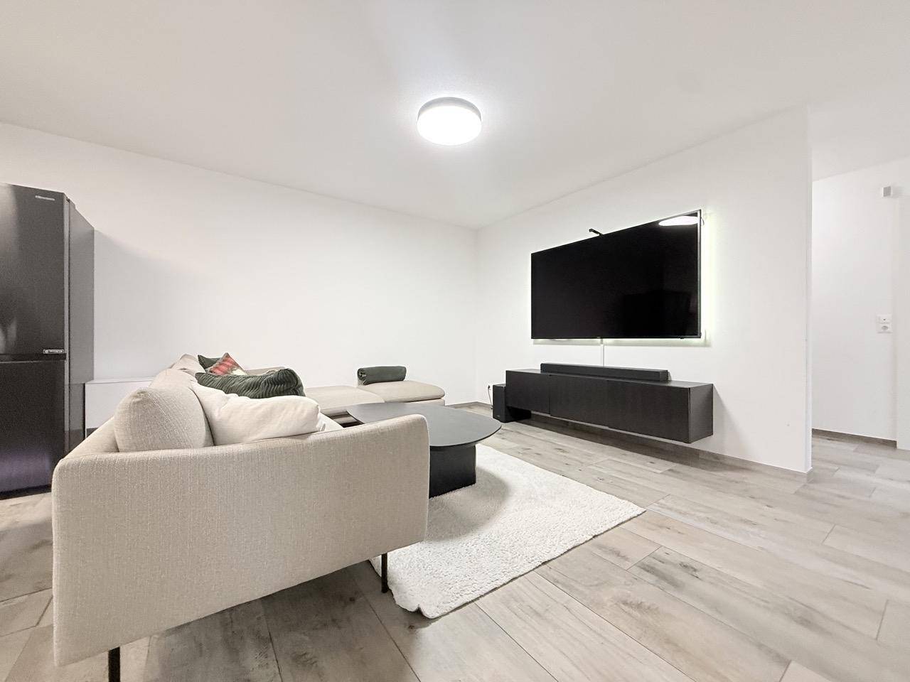 Gemütlicher Wohnbereich mit beigem Sofa, Couchtisch und großem Wandfernseher.