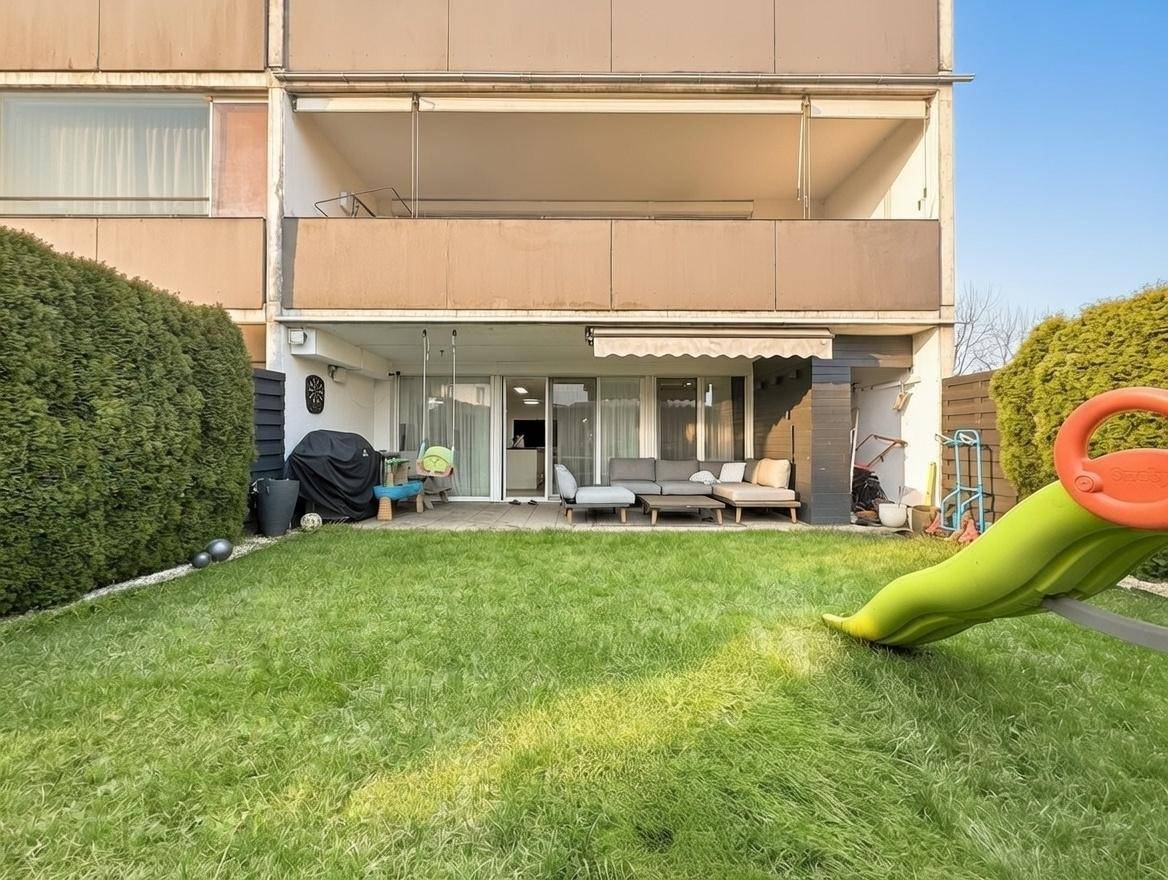 Gartenbereich mit Terrasse, Rasenfläche und Blick auf das Gebäude mit Balkonen.