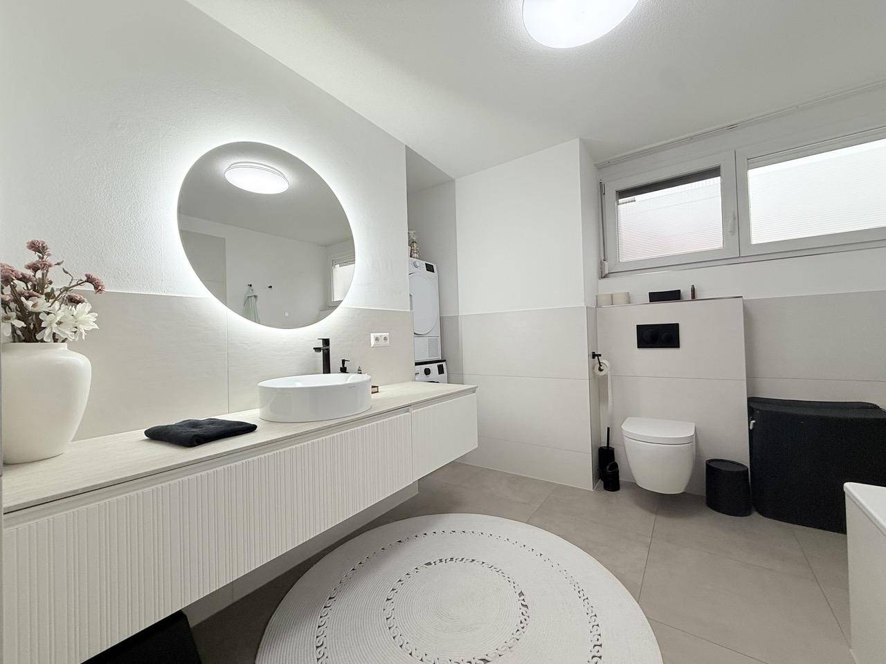 Modernes Badezimmer mit beleuchtetem Spiegel, Waschtisch und wandhängendem WC.