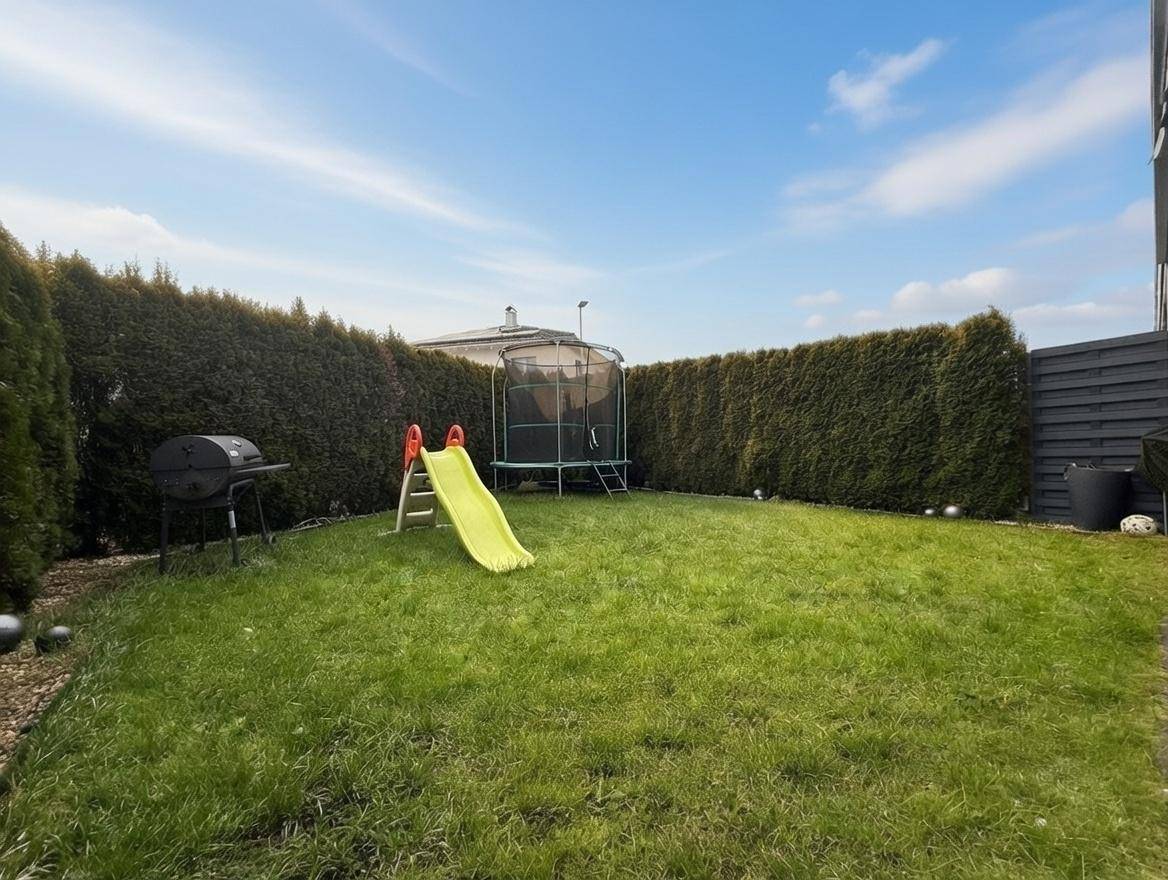 Gepflegter Garten mit Rasenfläche, Hecke, Grill und Kinderspielgeräten.