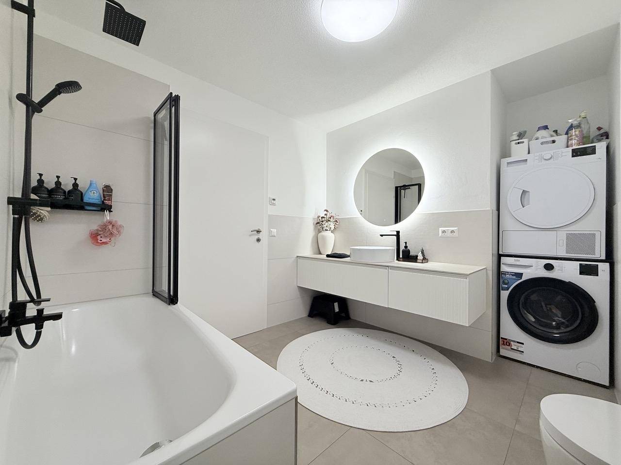 Modernes Badezimmer mit Badewanne, Dusche, Waschtisch und Waschmaschine.