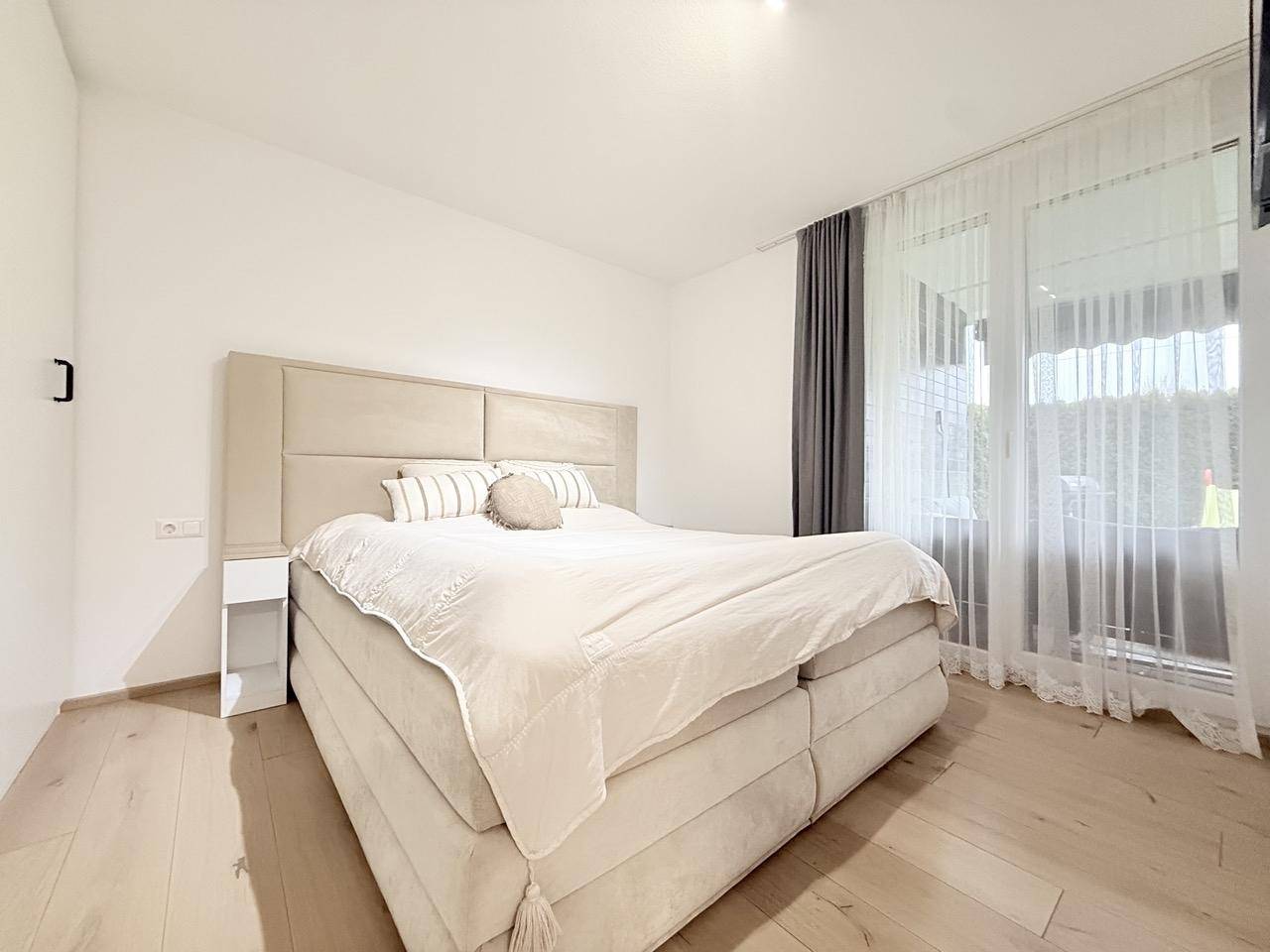 Helles Schlafzimmer mit großem Boxspringbett, Nachttischen und Zugang zum Balkon.