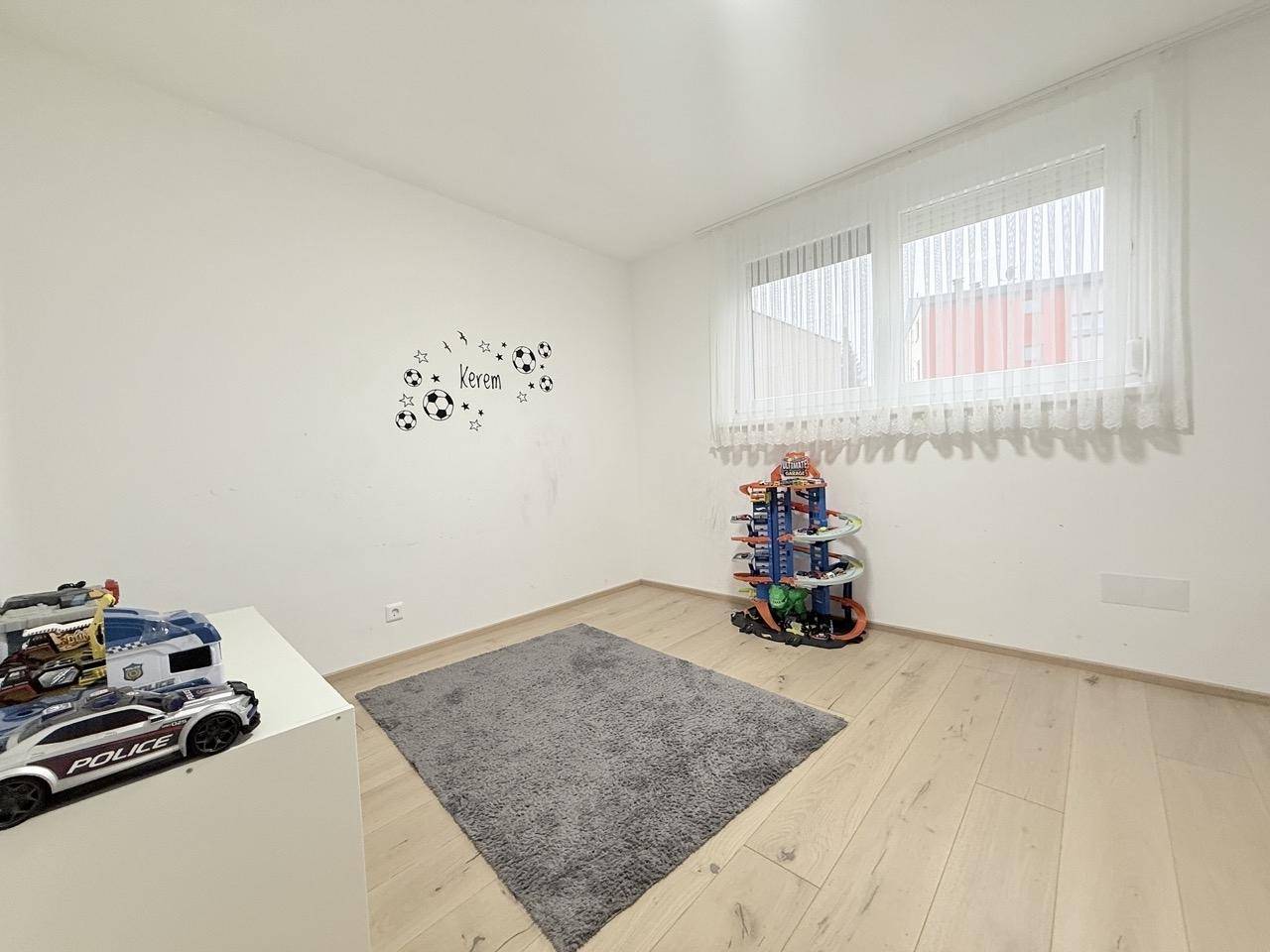 Kinderzimmer mit hellem Holzboden, Fenster und Spielzeug, bereit zum Einrichten.