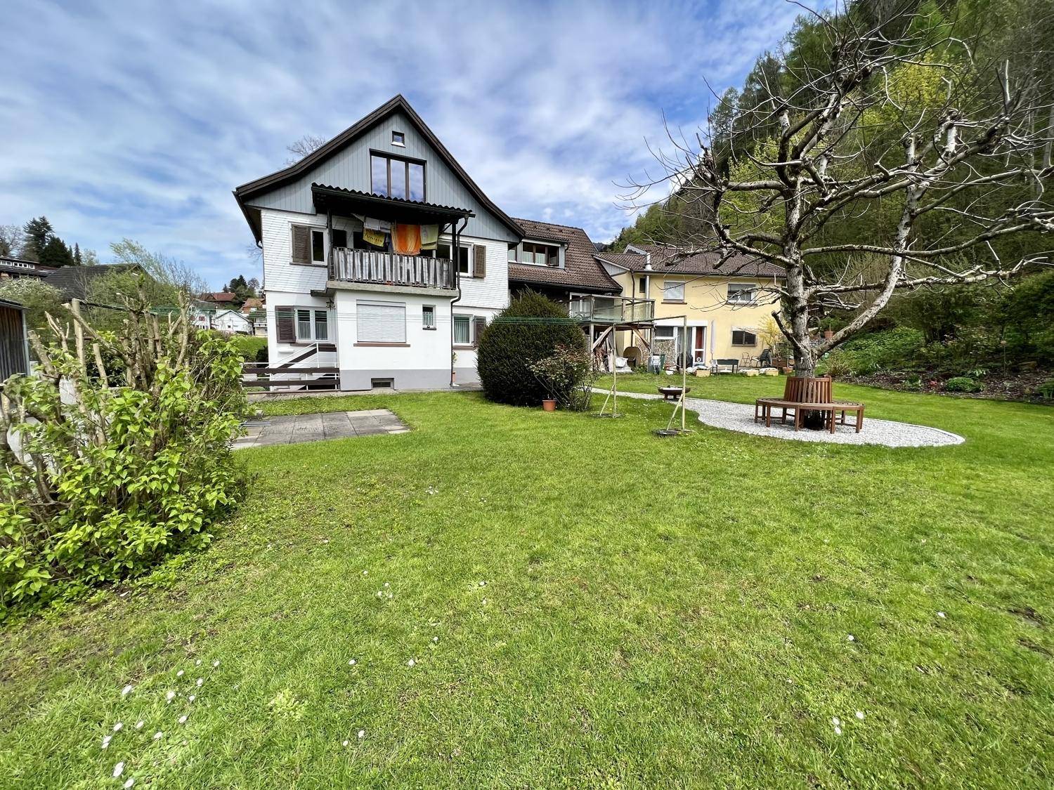 Großzügiger Gartenbereich mit Sitzbank und Blick auf das Mehrfamilienhaus.