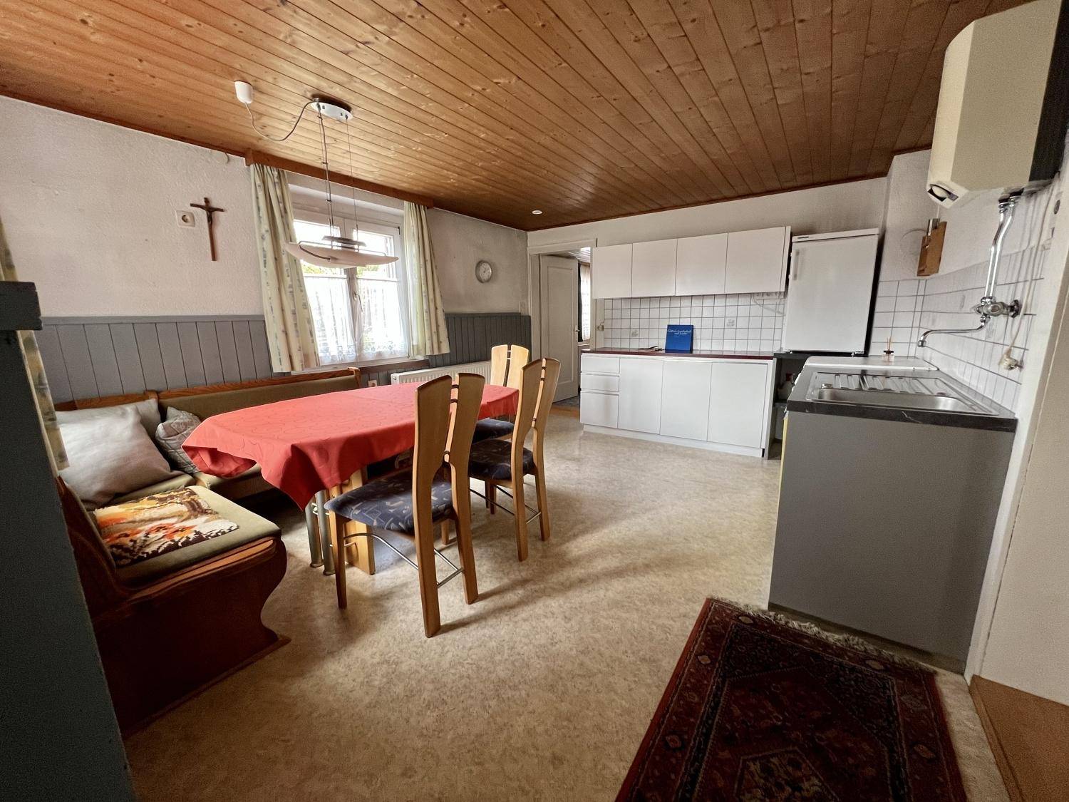 Gemütliche Wohnküche mit Holztäfelung, Essbereich und einfacher Küchenzeile.