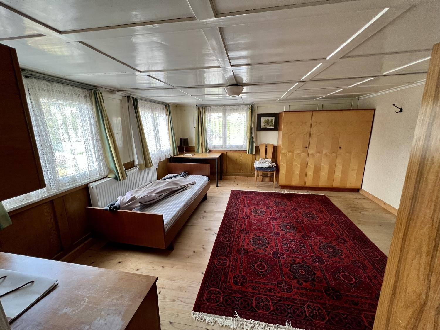 Schlafzimmer mit Holzboden, Holzmöbeln und mehreren Fenstern für viel Licht.