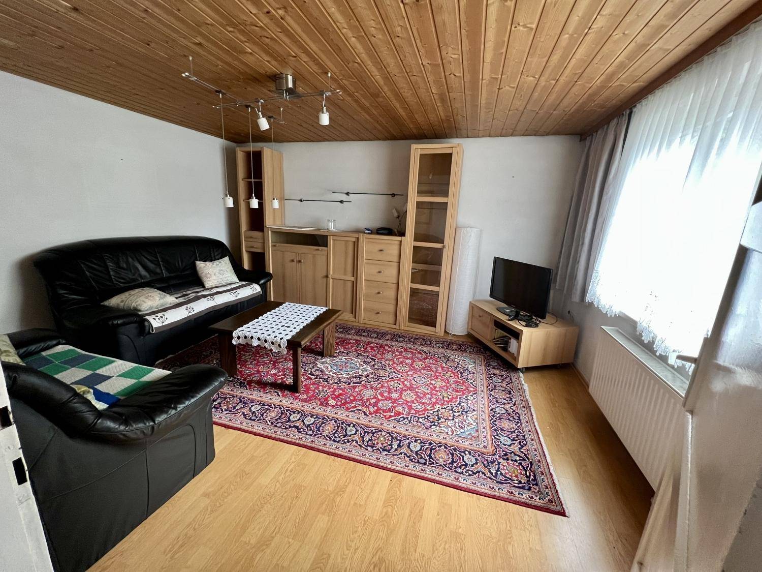 Wohnzimmer mit Holzboden, Teppich und traditionellen Holzmöbeln.