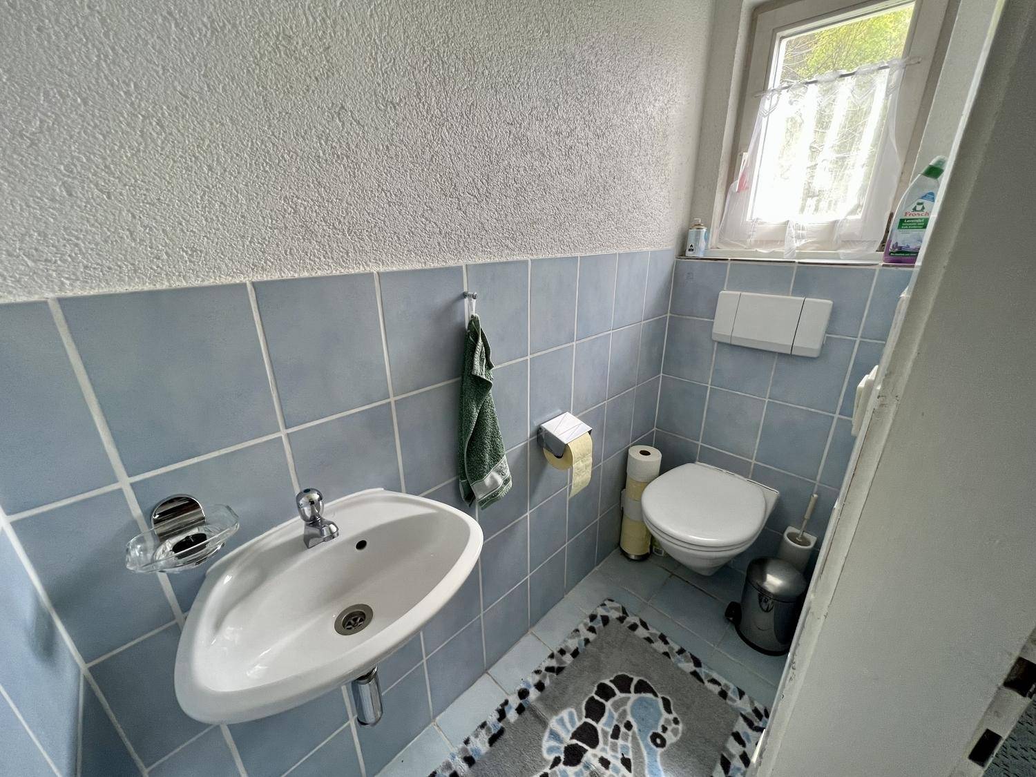 Kleines Gäste-WC mit blauen Fliesen, Fenster und Waschbecken.