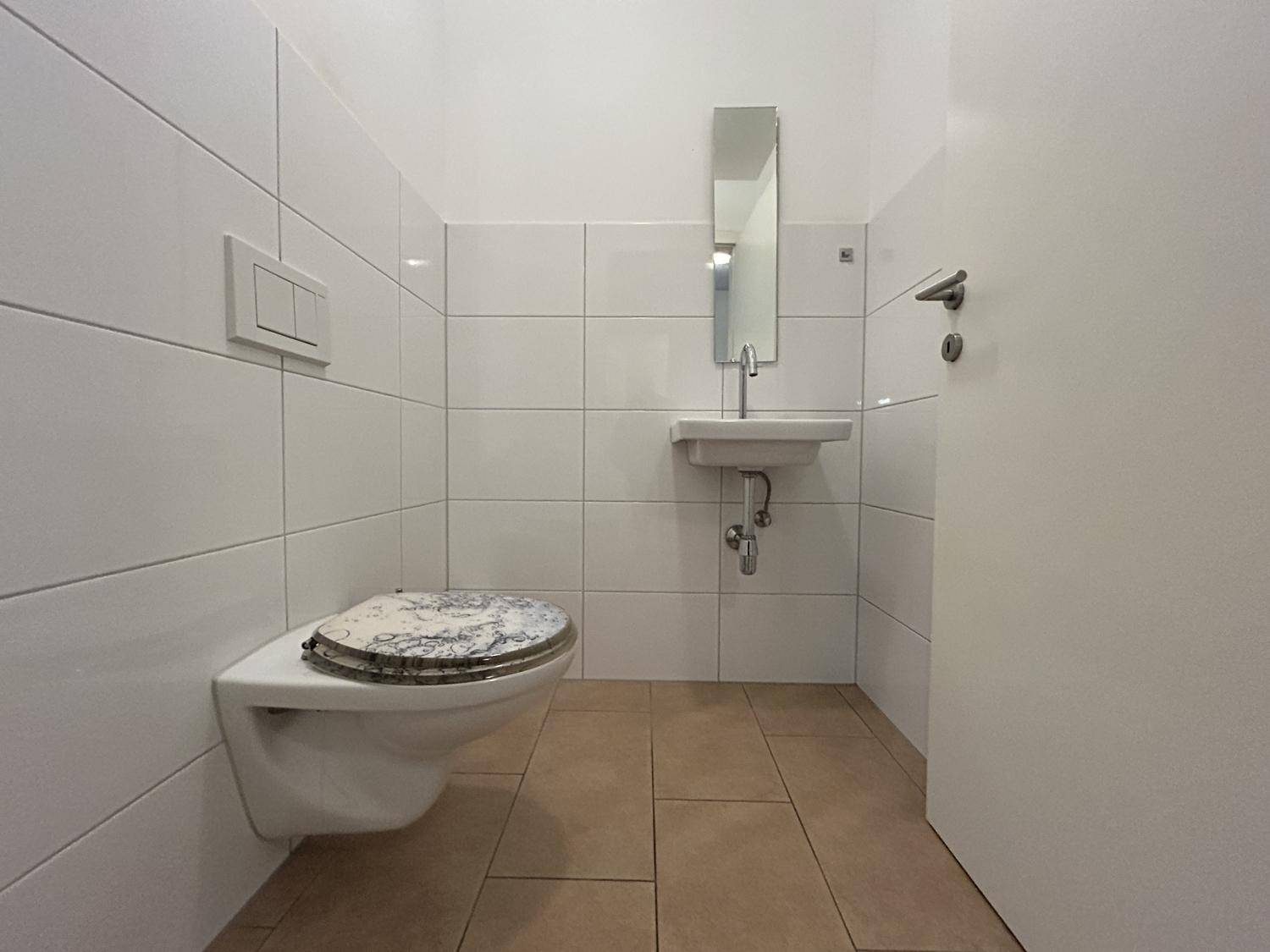 Gäste-WC mit weißen Wandfliesen, wandhängendem WC und kleinem Waschbecken.