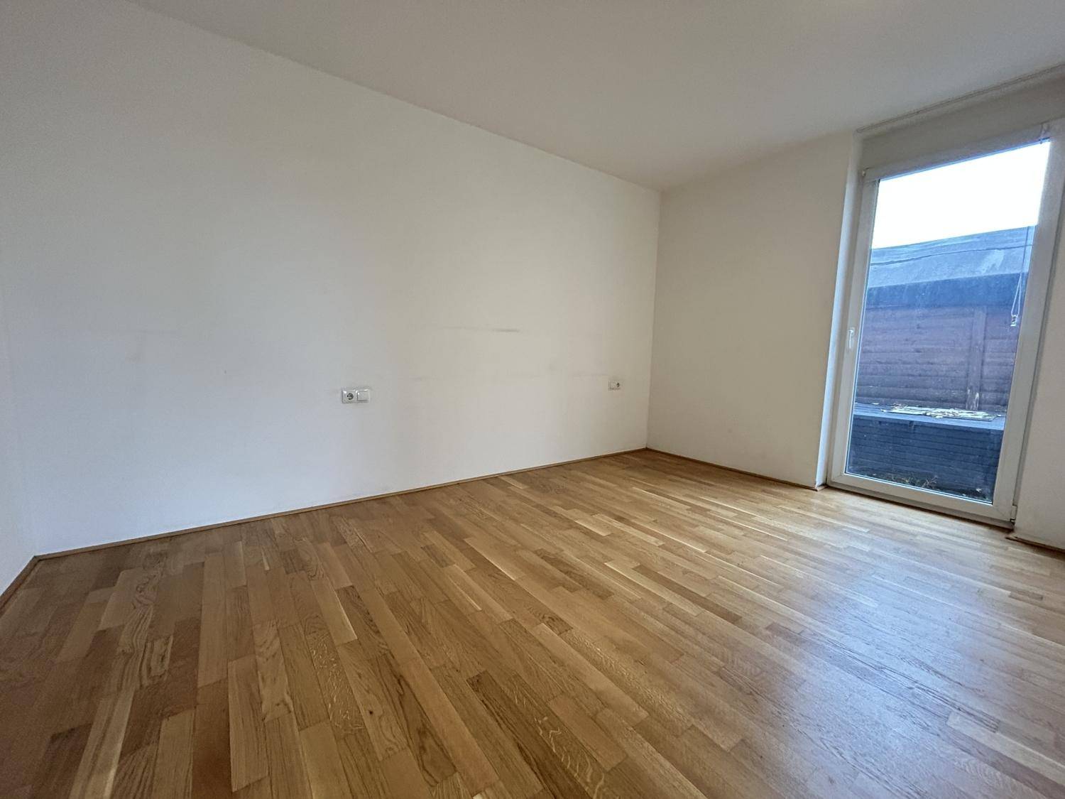 Geräumiges Schlafzimmer mit Holzboden und großem Fenster, das viel Tageslicht hereinlässt.