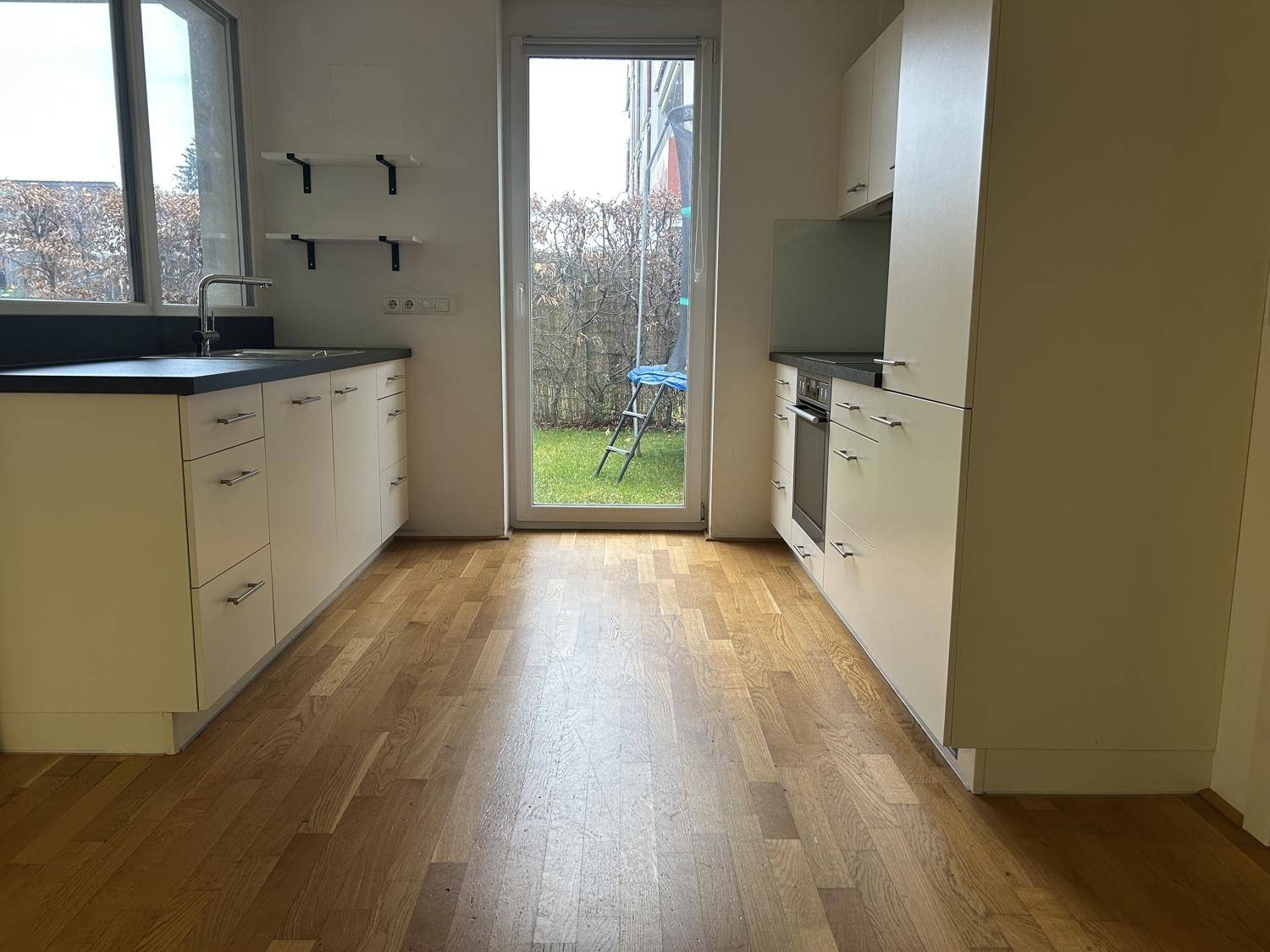 Moderne Küche mit hellen Schränken, dunkler Arbeitsplatte und Holzboden mit Gartenzugang.