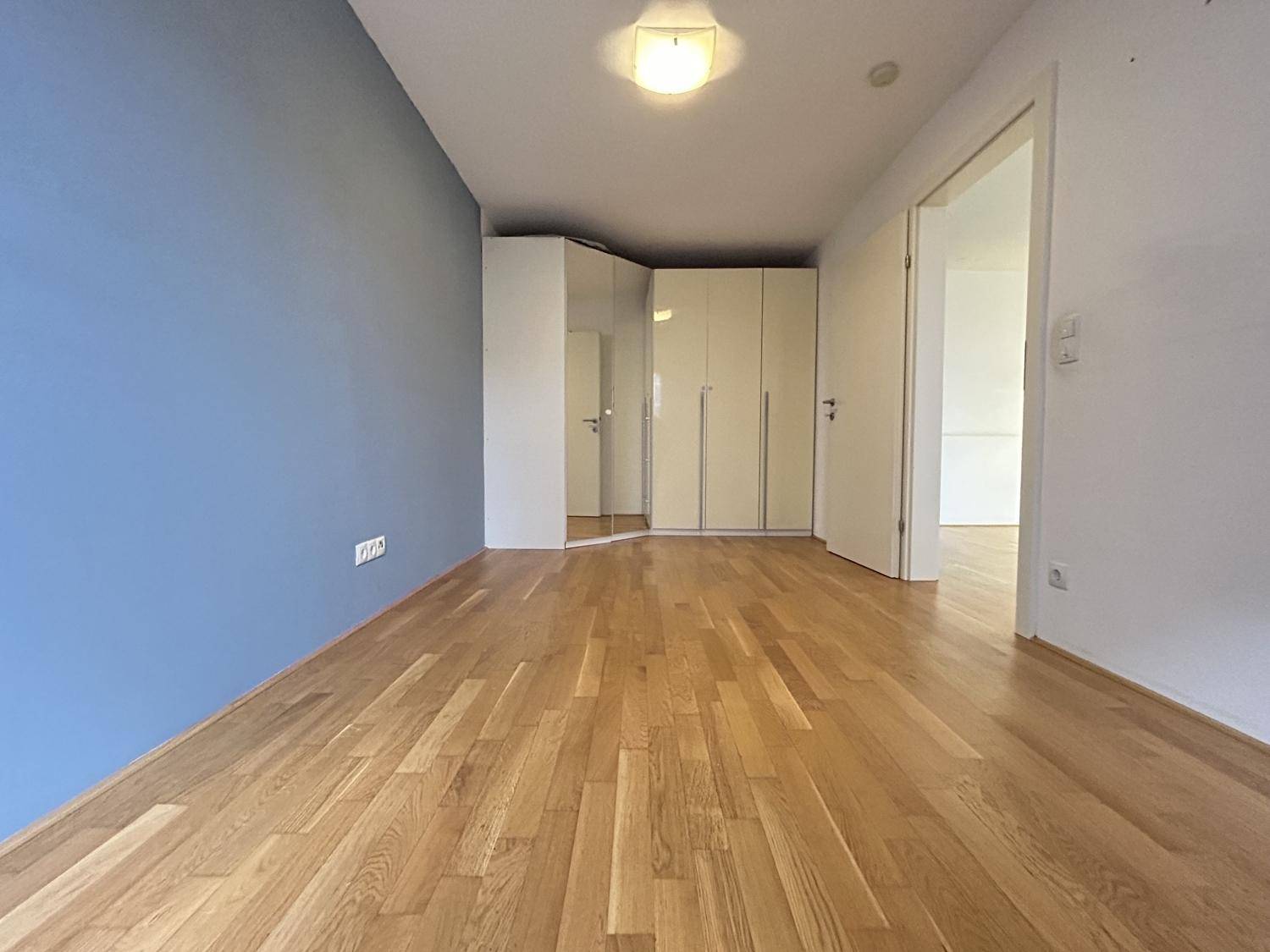 Schlafzimmer mit Holzboden, einer blauen Akzentwand und praktischen Einbauschränken.