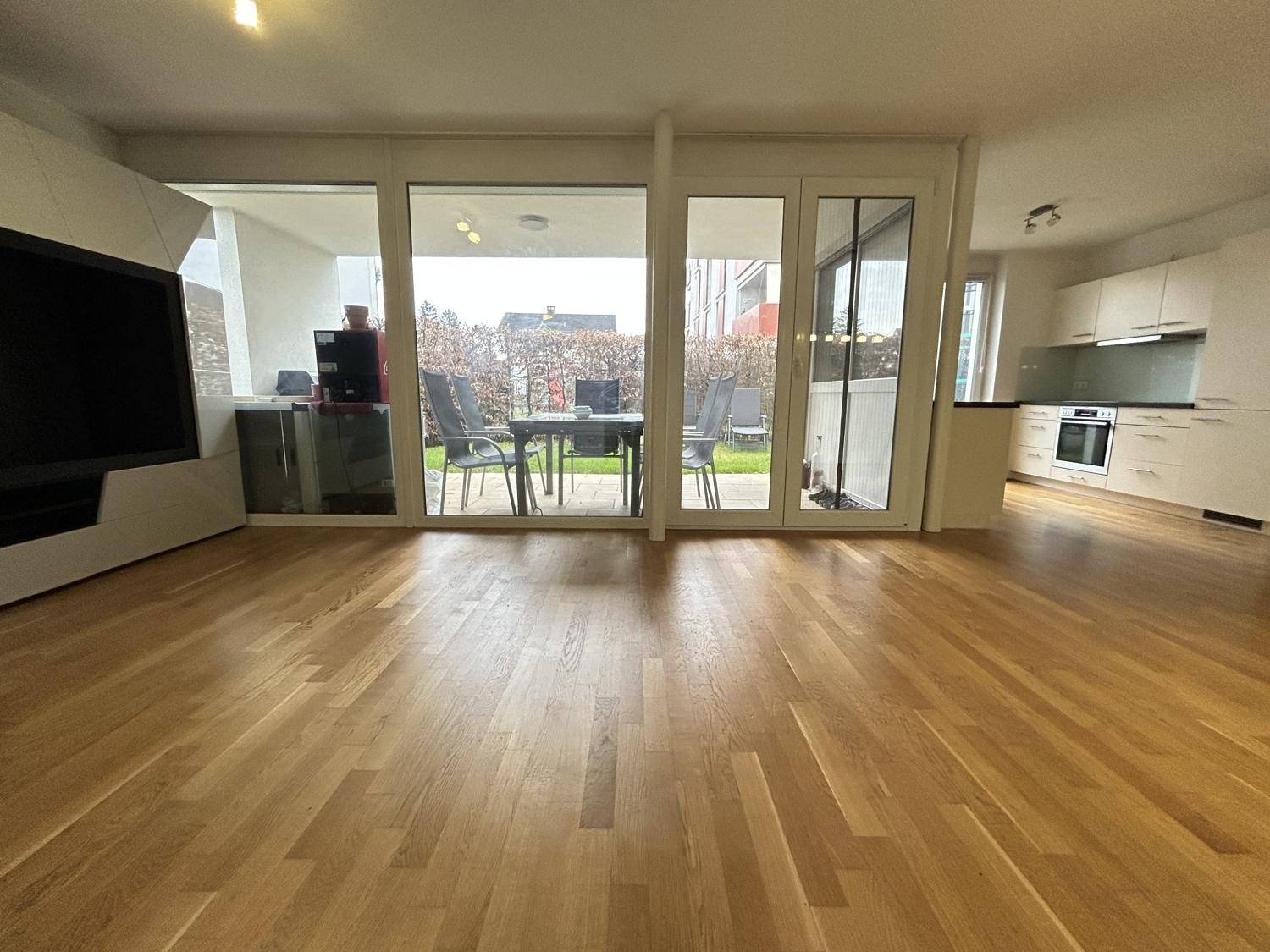 Offener Wohn- und Essbereich mit Holzboden und Zugang zur Terrasse durch große Fenster.