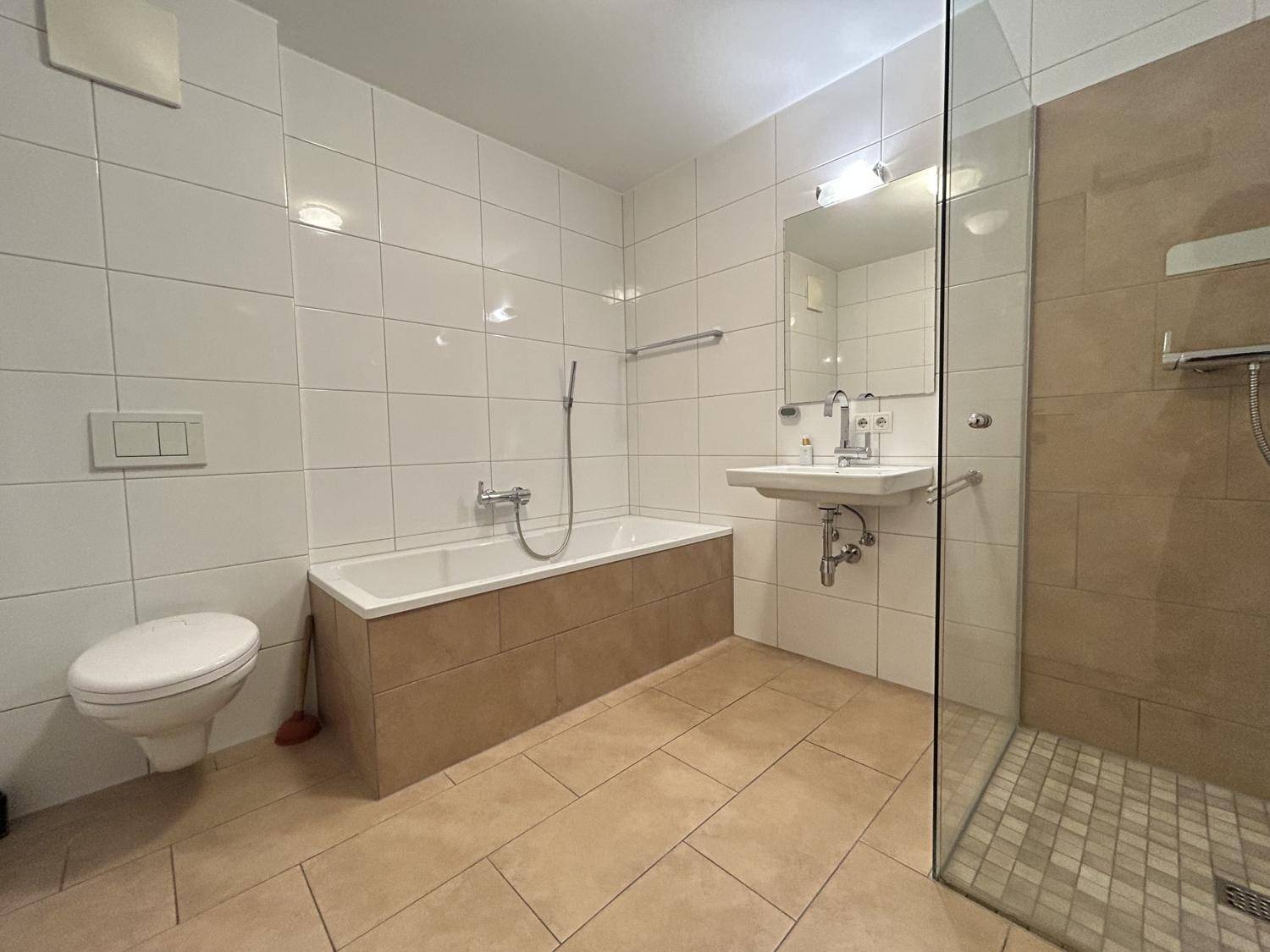 Helles Badezimmer mit Badewanne, ebenerdiger Dusche, WC und Waschbecken.