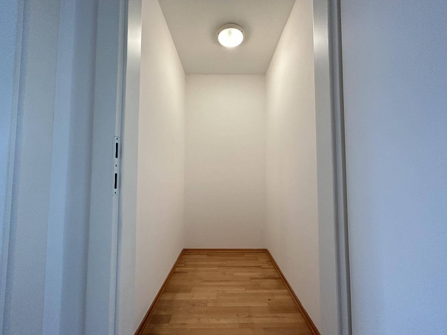 Kleiner, heller Abstellraum mit Holzparkettboden und weißen Wänden, ideal für Lagerzwecke.