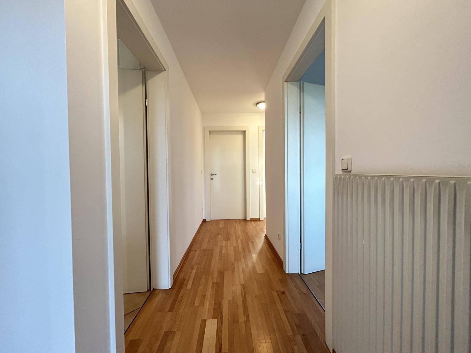Heller Flur mit warmem Holzparkettboden und weißen Wänden, der zu weiteren Räumen führt.