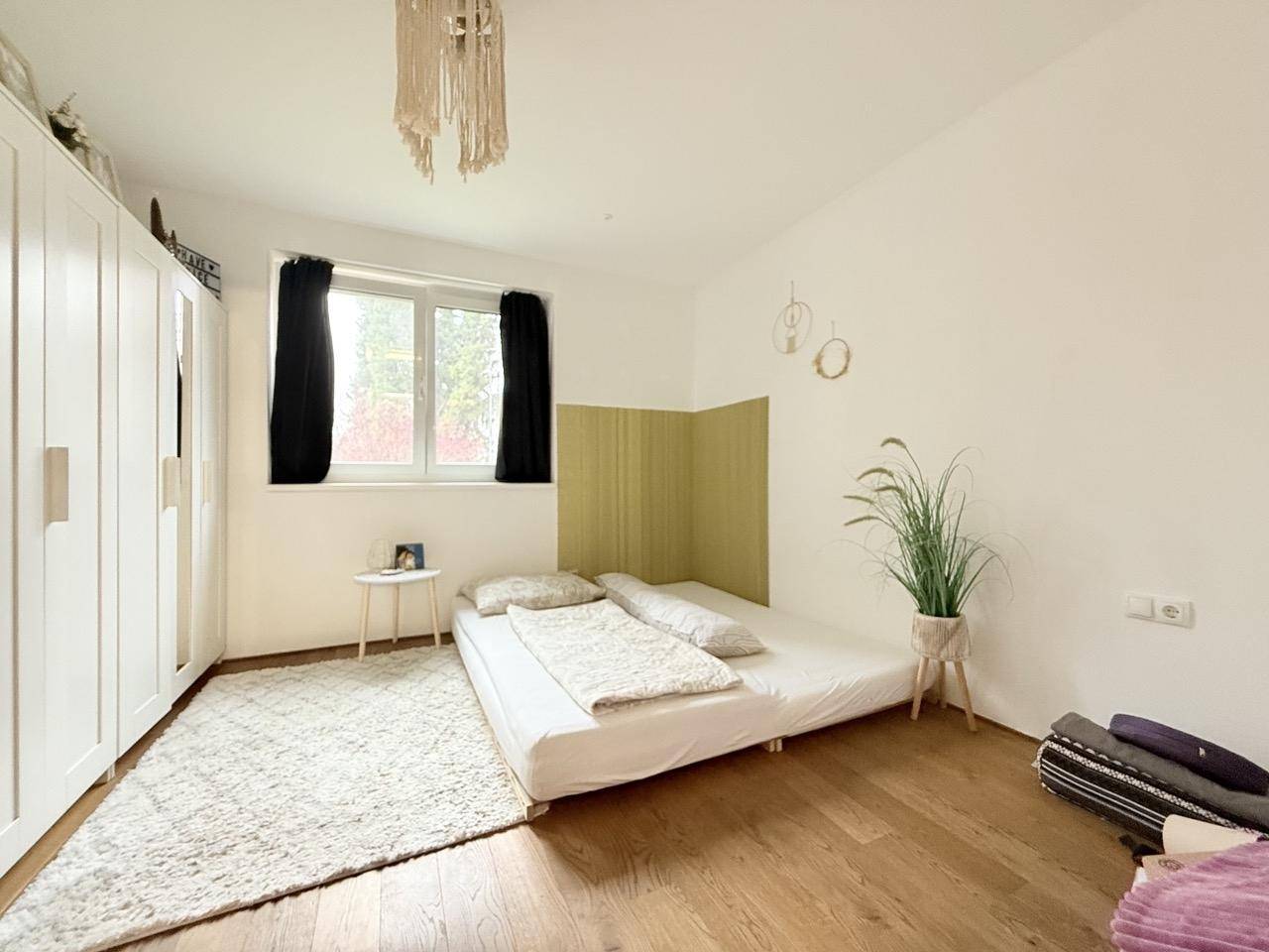 Schlafzimmer mit Holzboden, weißem Kleiderschrank und Blick ins Grüne.