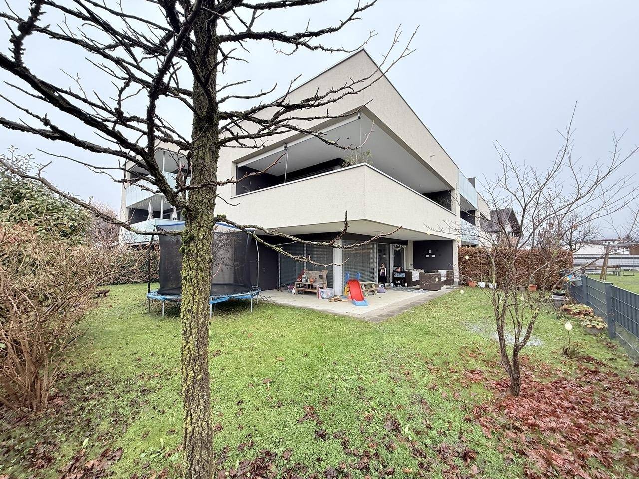 Hinterhof mit Rasen, Trampolin und Terrasse vor der modernen Wohnanlage.