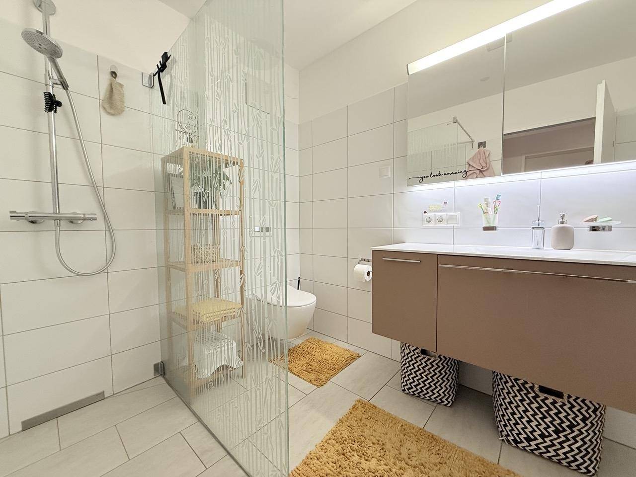 Helles Badezimmer mit großer Dusche, modernem Waschtisch und Spiegelschrank.