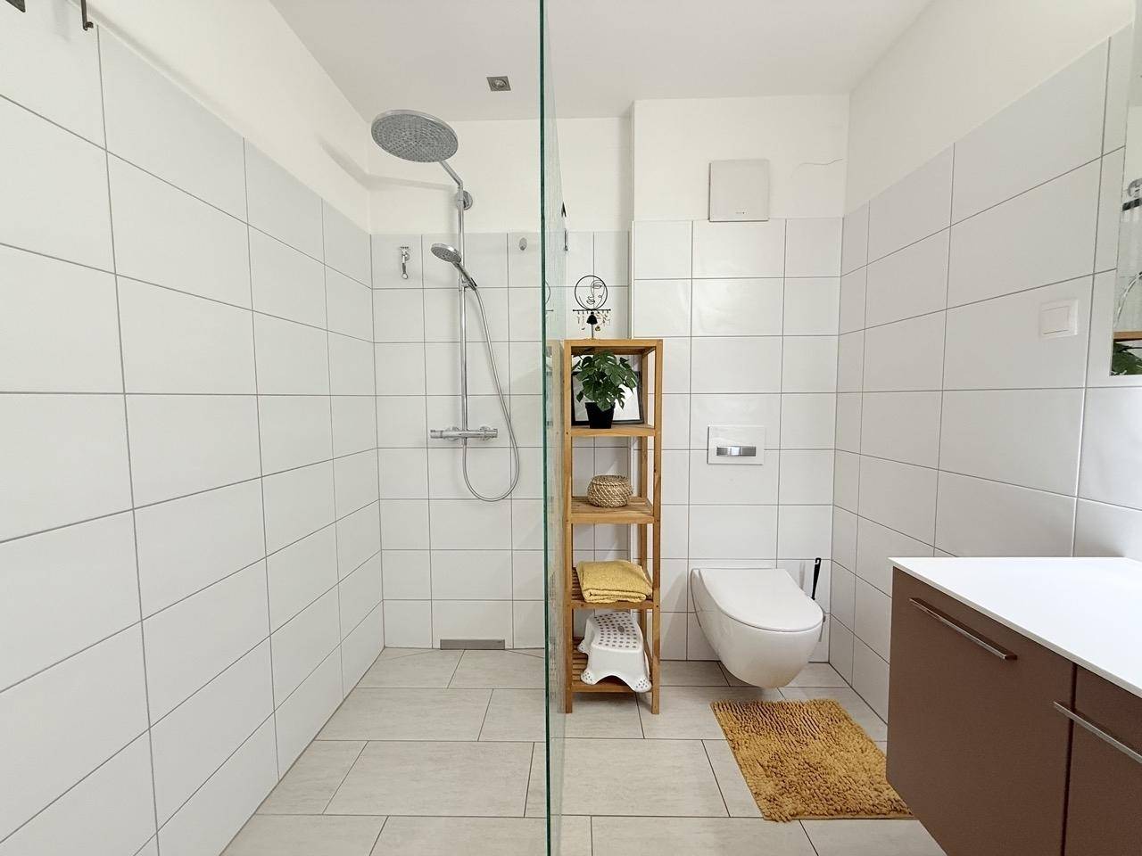 Modernes Badezimmer mit ebenerdiger Dusche, Wand-WC und hellen Fliesen.