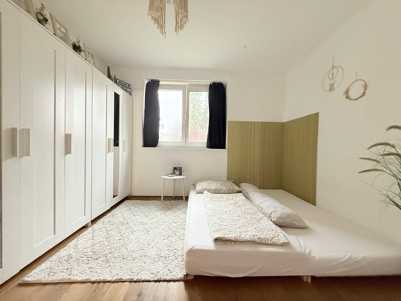 Schlafzimmer mit Holzboden, großem Kleiderschrank und Fenster mit Blick ins Grüne.