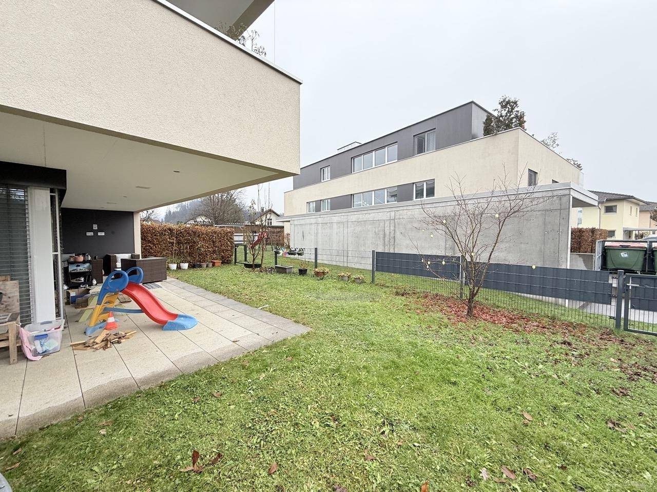 Gartenbereich mit Rasenfläche, Terrasse und Kinderrutsche neben dem Gebäude.
