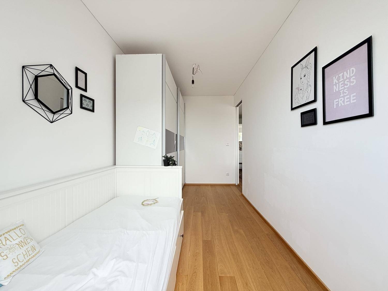 Helles Schlafzimmer mit Holzboden, weißem Bett und moderner Wanddekoration.