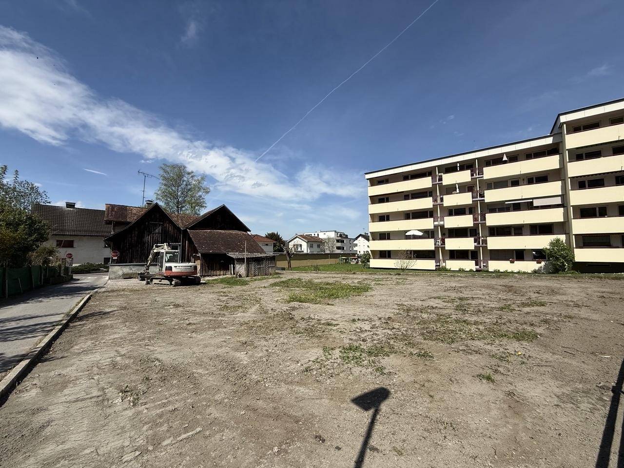 Freies Grundstück mit Blick auf ein älteres Gebäude und ein Mehrfamilienhaus im Hintergrund.