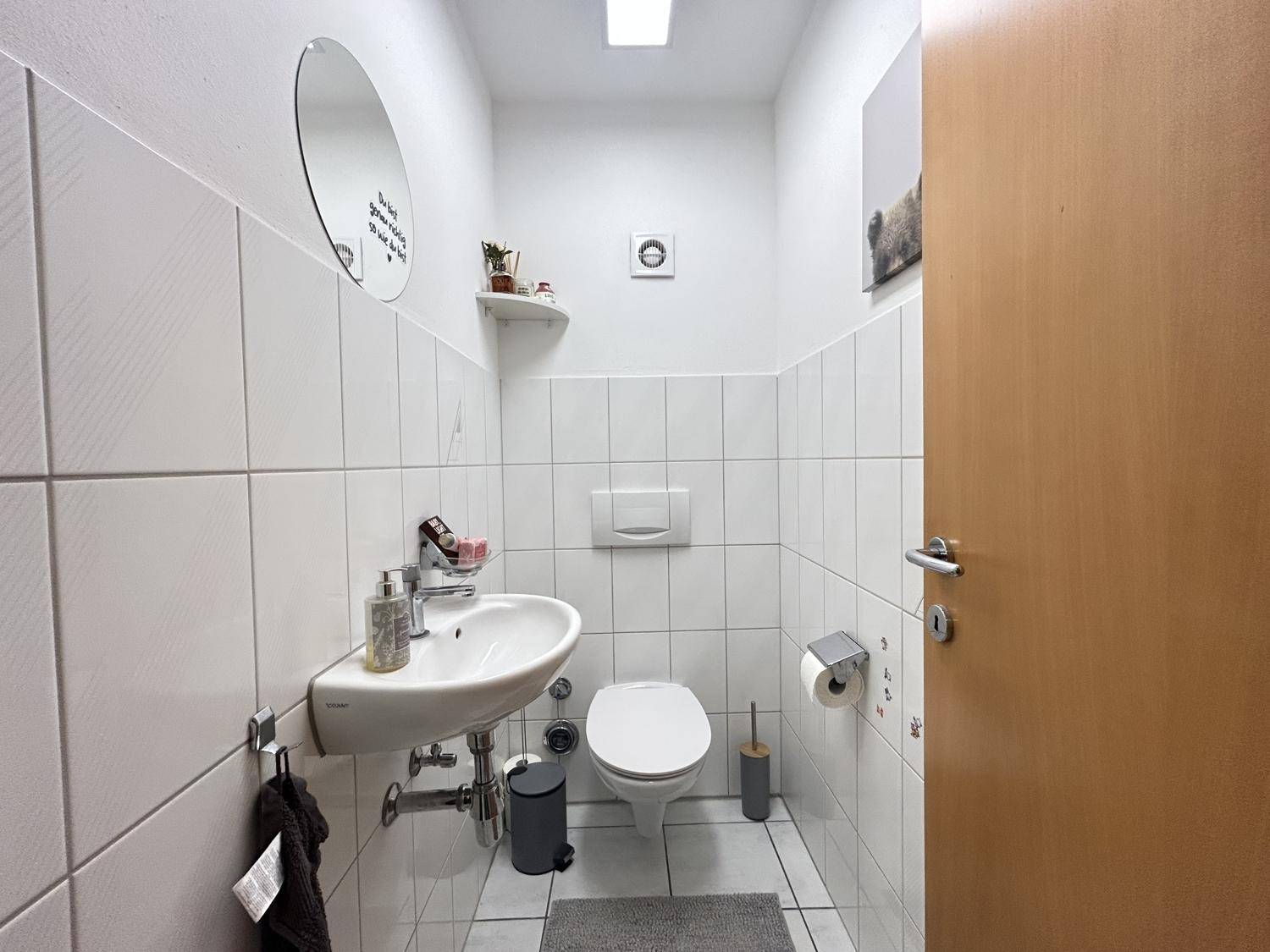 Helles Gäste-WC mit weißen Fliesen, wandhängendem WC und kleinem Waschbecken.
