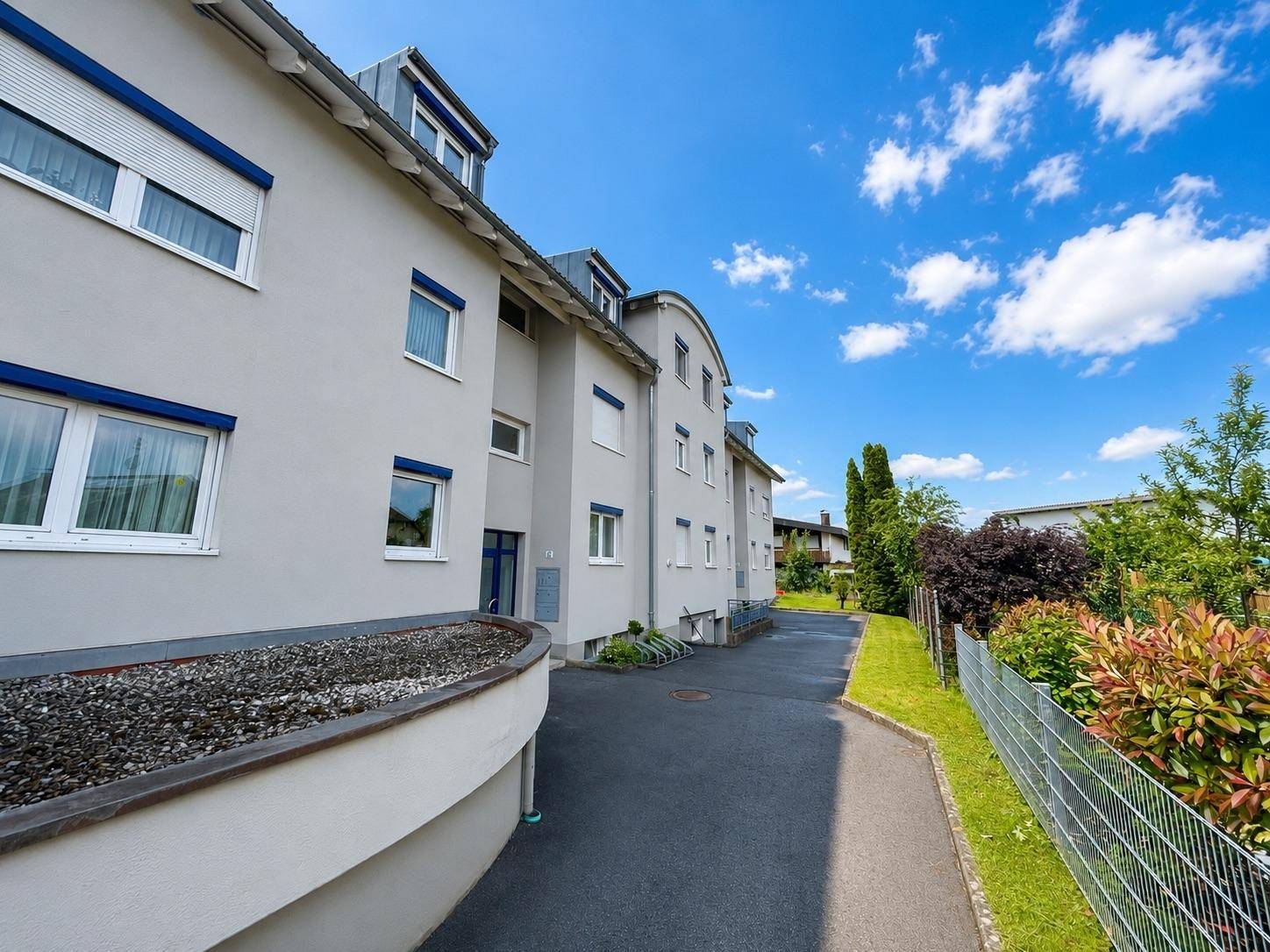 Ansicht der modernen Gebäudefassade mit blauen Fensterläden und gepflegter Außenanlage.