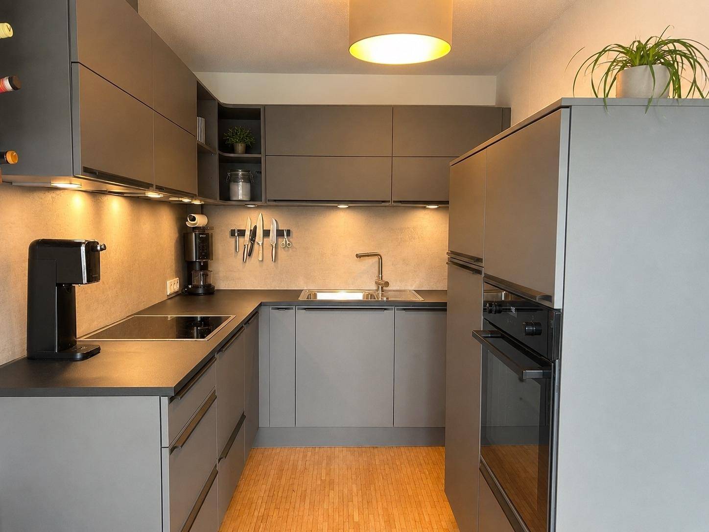 Moderne U-förmige Küche mit grauen Schränken, integrierten Geräten und dunklen Arbeitsplatten.