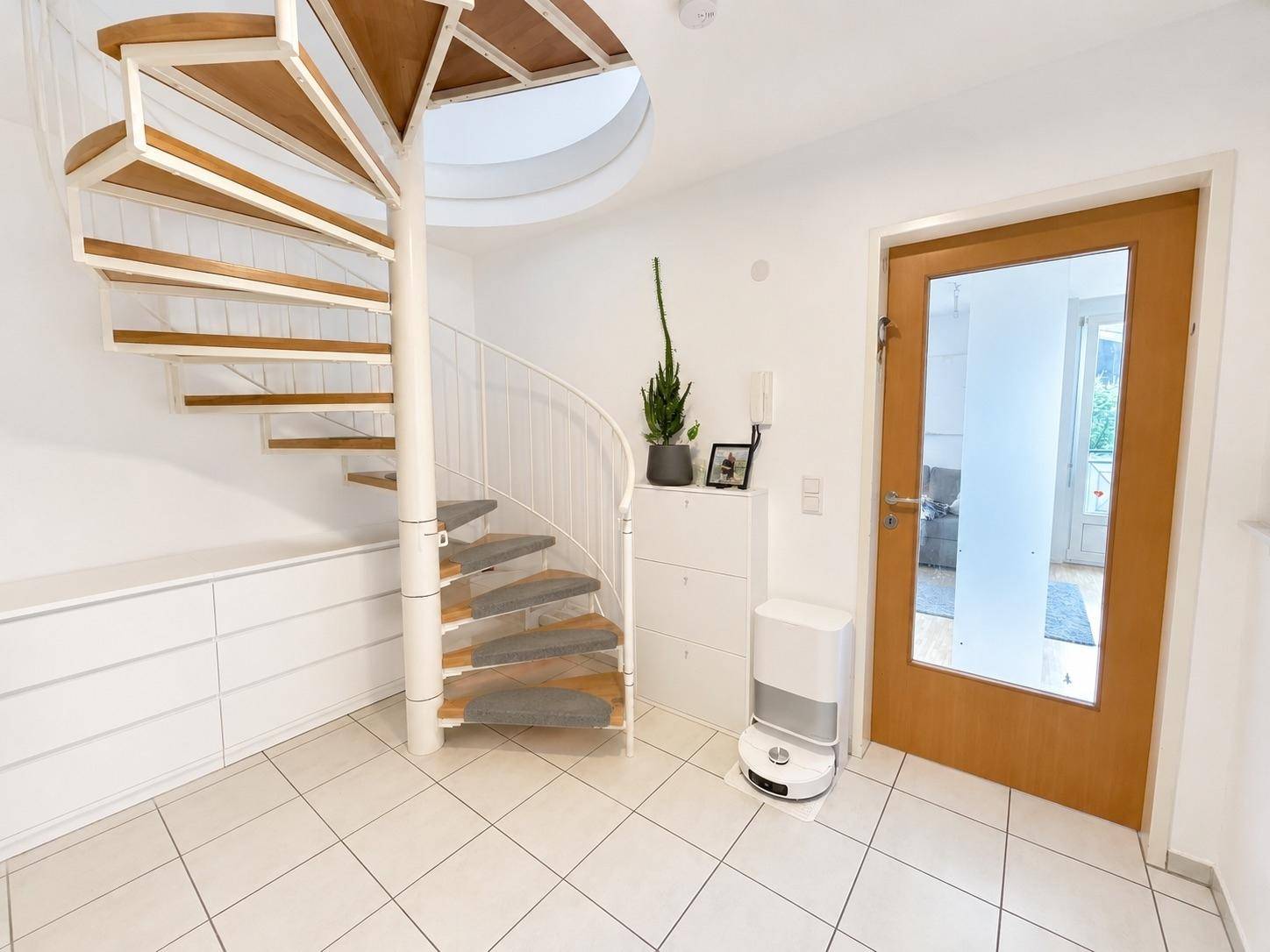 Heller Eingangsbereich mit eleganter Wendeltreppe, weißen Fliesenboden und Holztür.