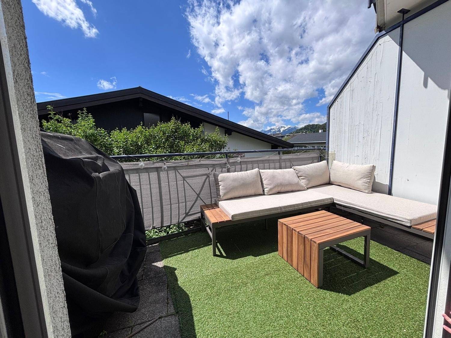 Sonnenbalkon mit Kunstrasen, bequemen Gartenmöbeln und Bergblick in der Ferne.