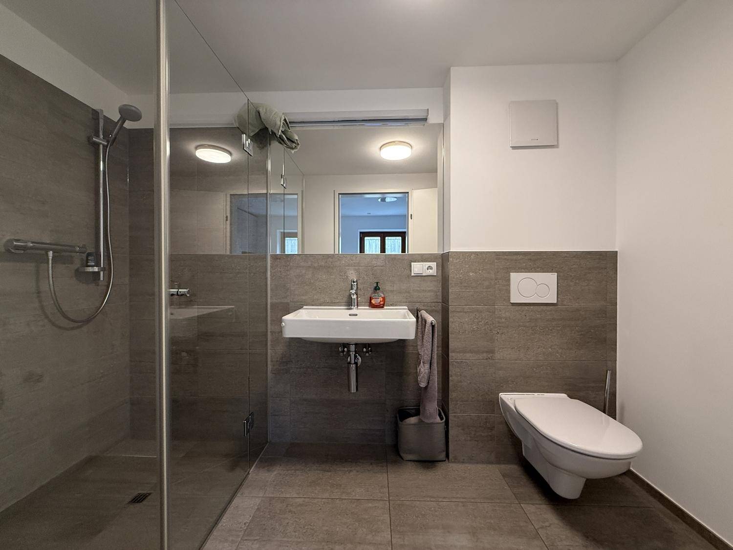 Modernes Badezimmer mit ebenerdiger Glasdusche, Wand-WC und eleganten grauen Fliesen.