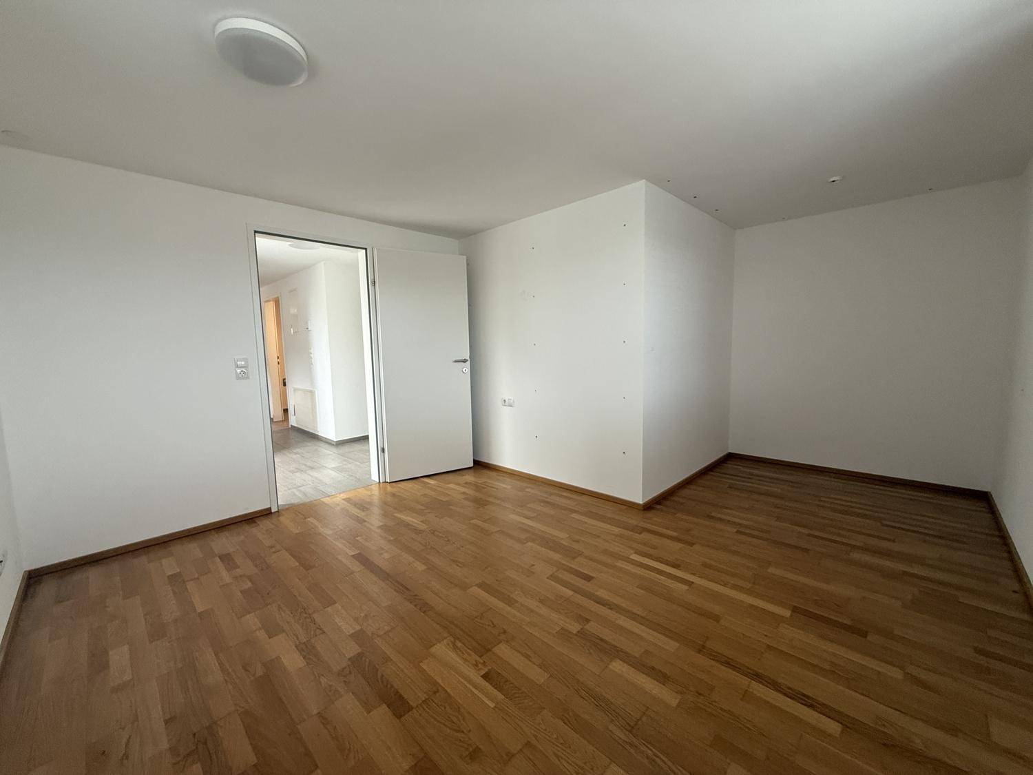 Geräumiges Schlafzimmer mit warmem Parkettboden und offenem Zugang zu einem angrenzenden Raum.
