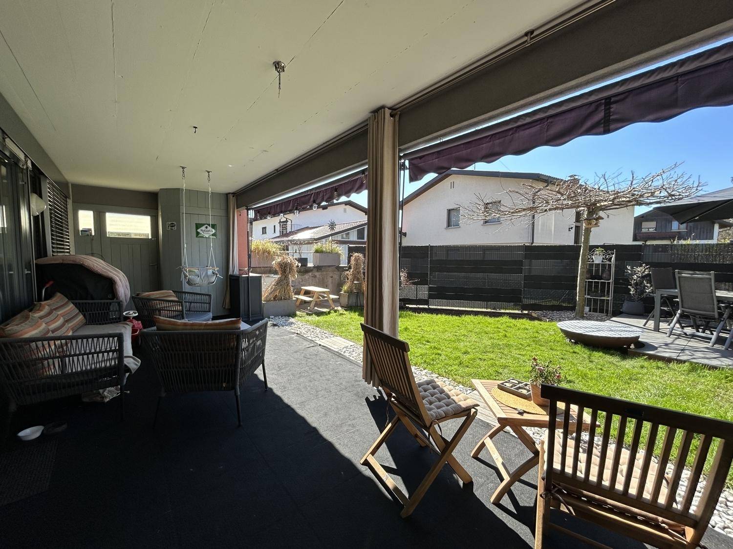 Überdachte Terrasse mit Holzmöbeln und direktem Zugang zum grünen Garten.